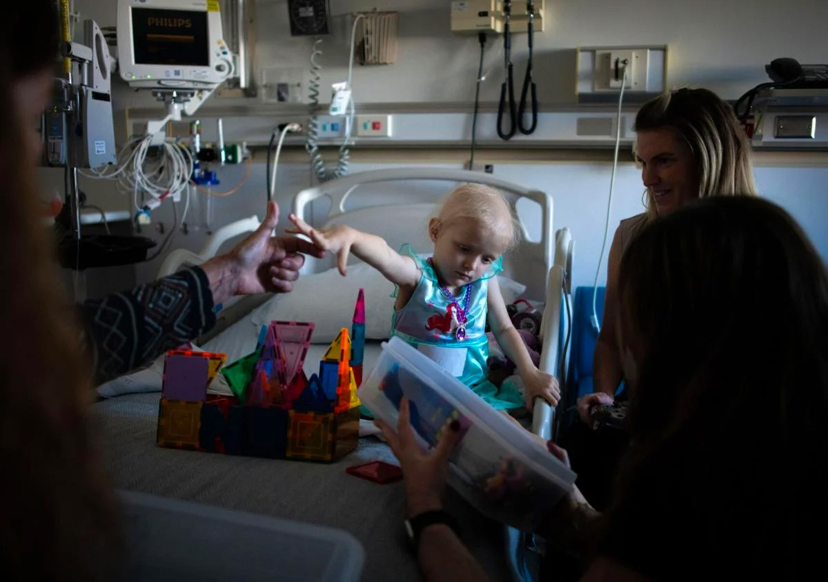 Parker reaches for the hand of her grandma, Penny Gaitan, while waiting for anti-nausea medication during her 10th week of chemotherapy treatment.