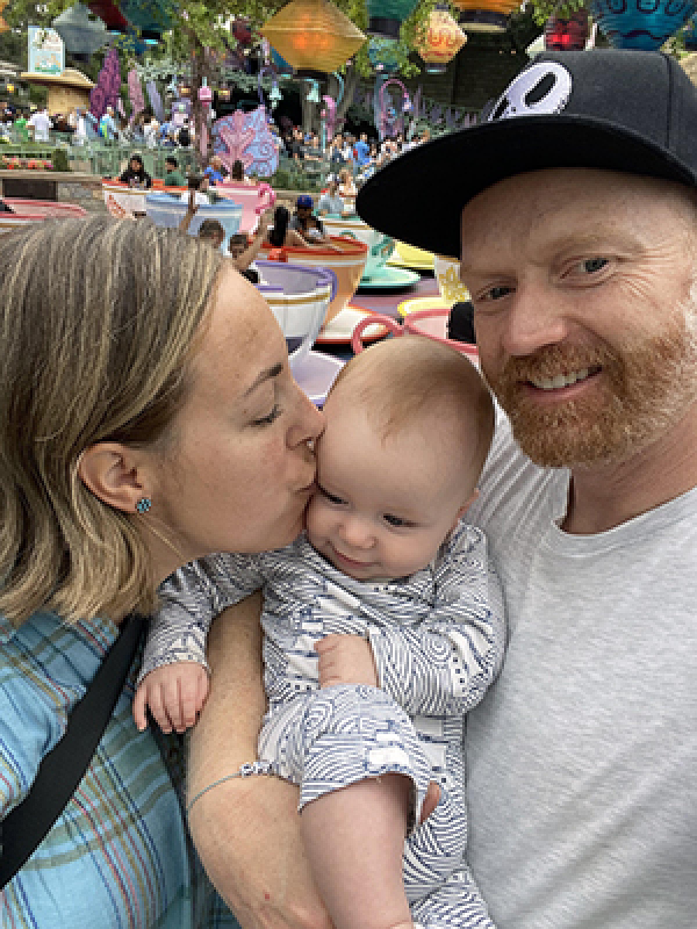 Brandon Plewe and his wife holding a baby while she kisses the baby's face