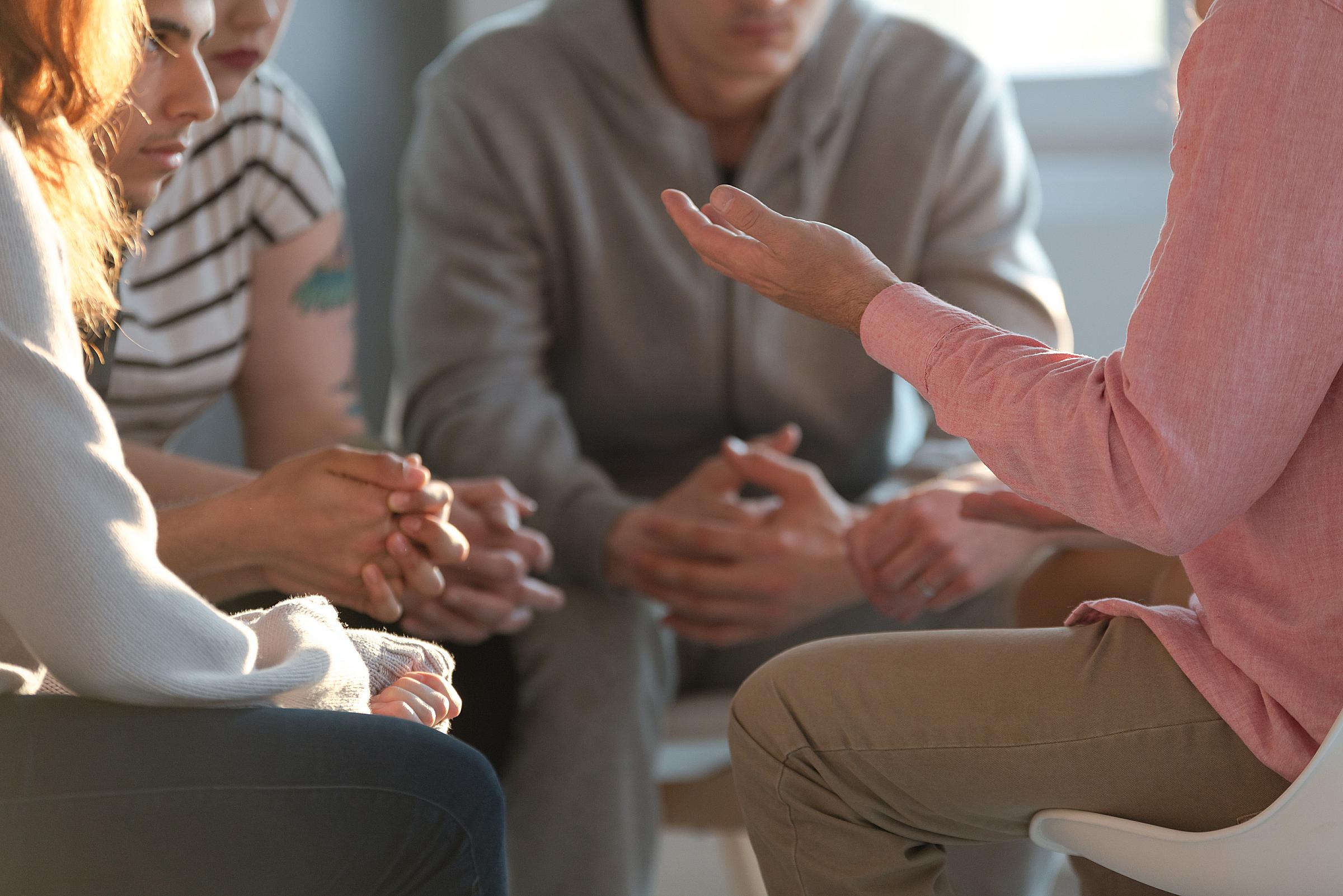 Group of young adults sitting in a circle, one gesturing with his hands