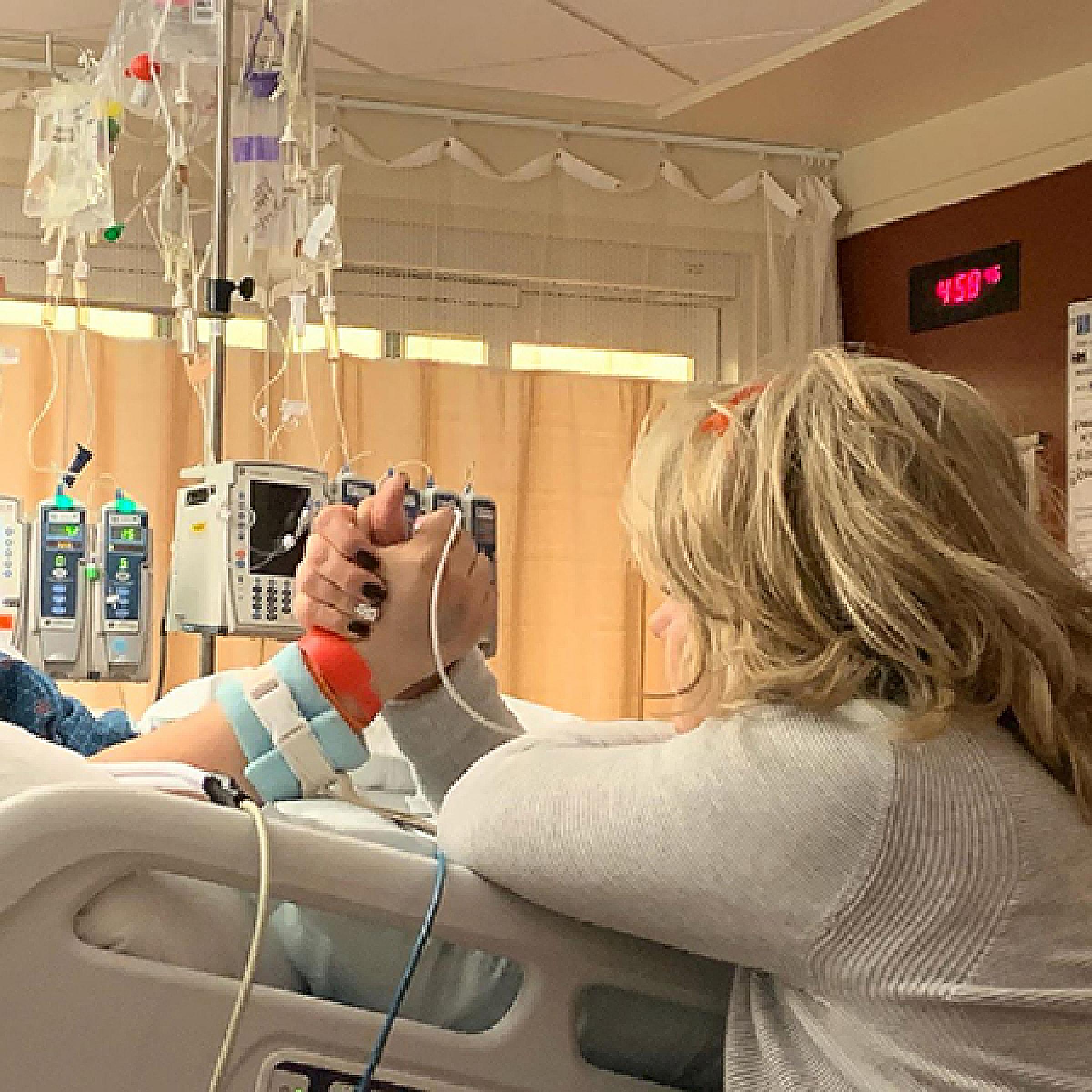 Kelli holding Ashley's hand while Ashley is in a hospital bed