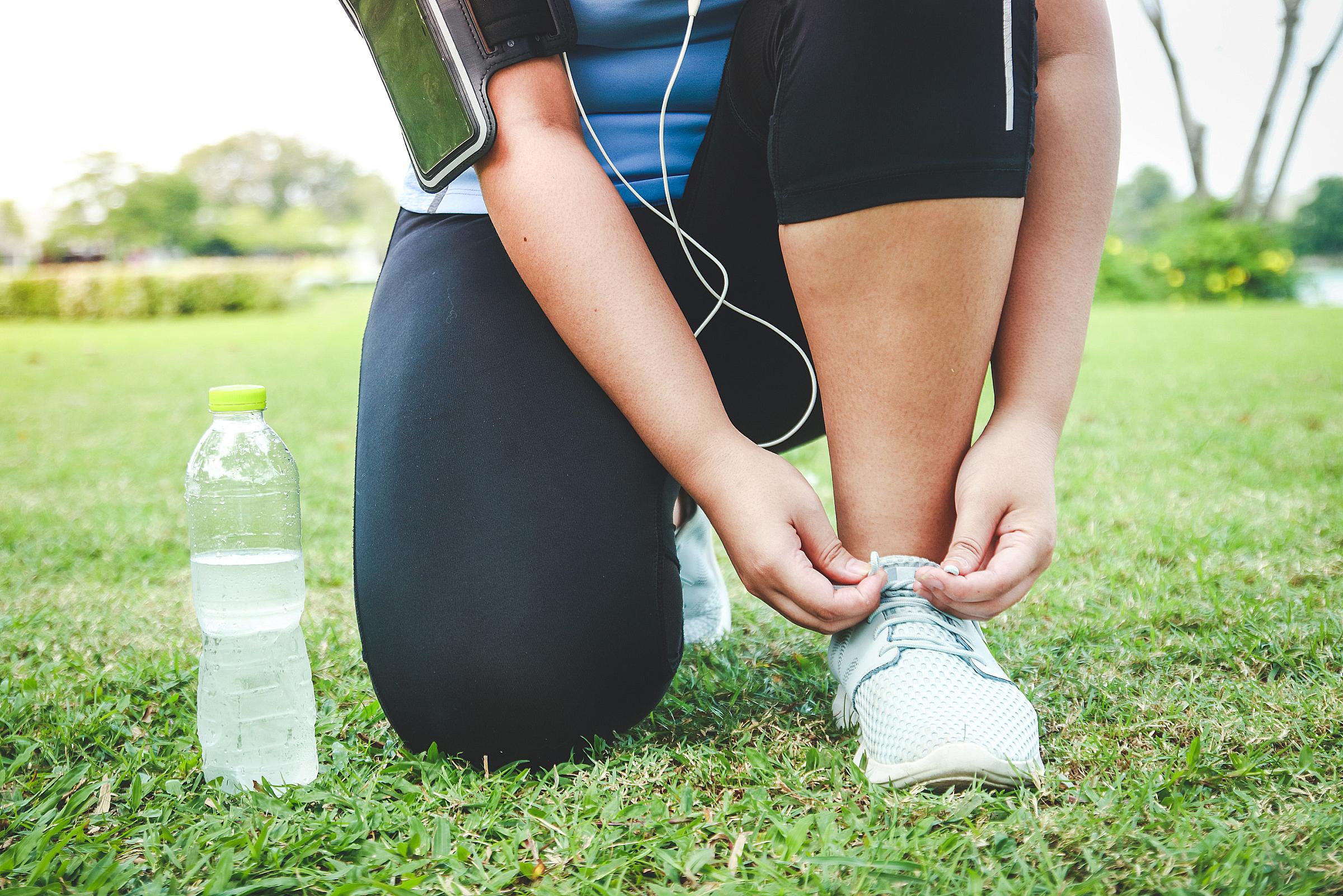 Woman in jogging clothes kneeling on grass to tie her shoe