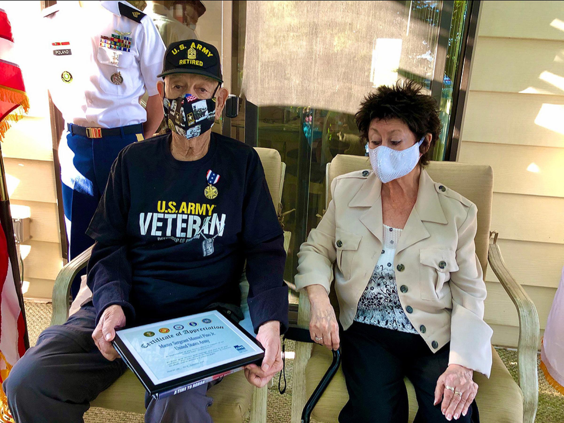 Manuel and his wife sitting on a porch while he holds a certificate