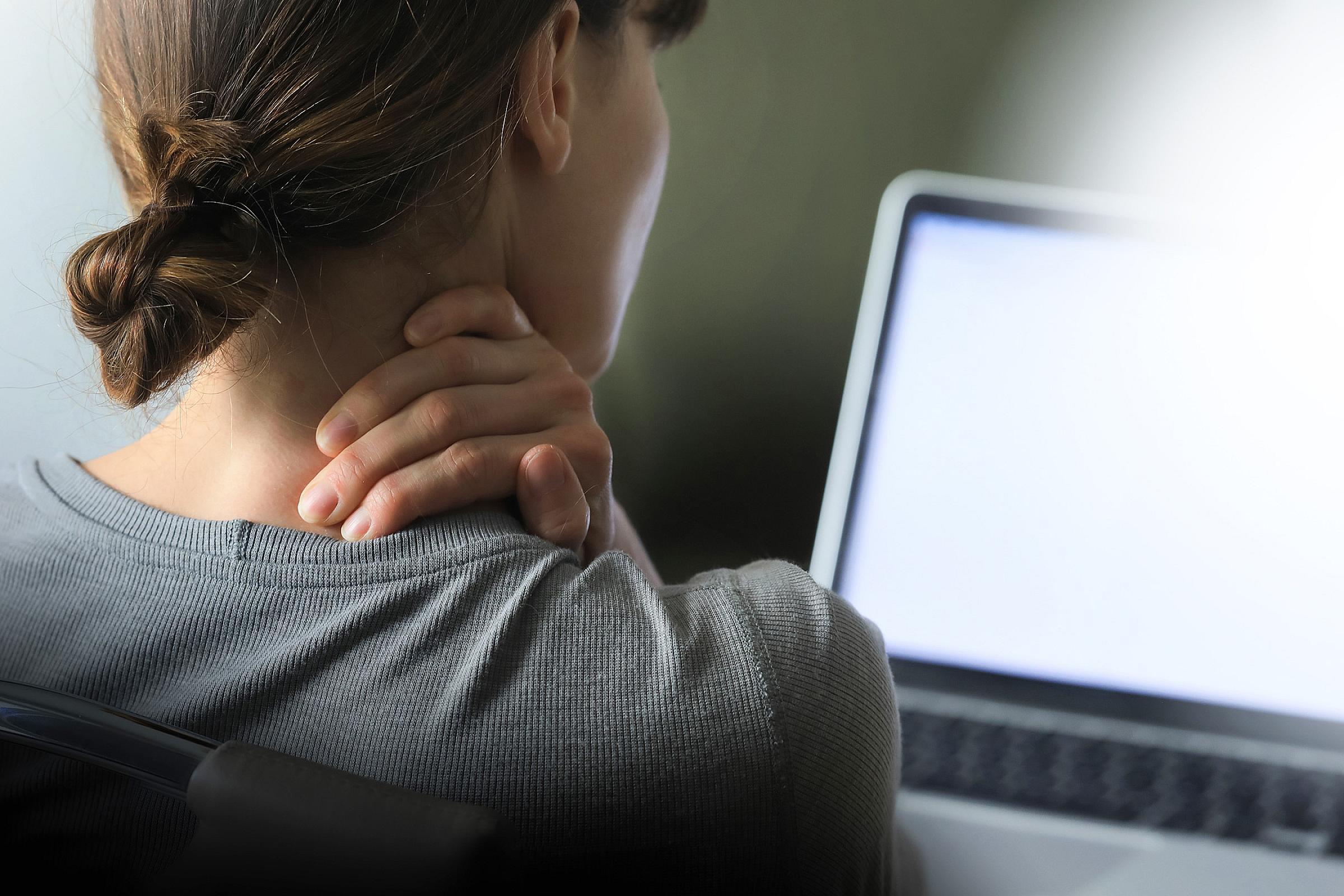 Woman holding her neck while looking at laptop