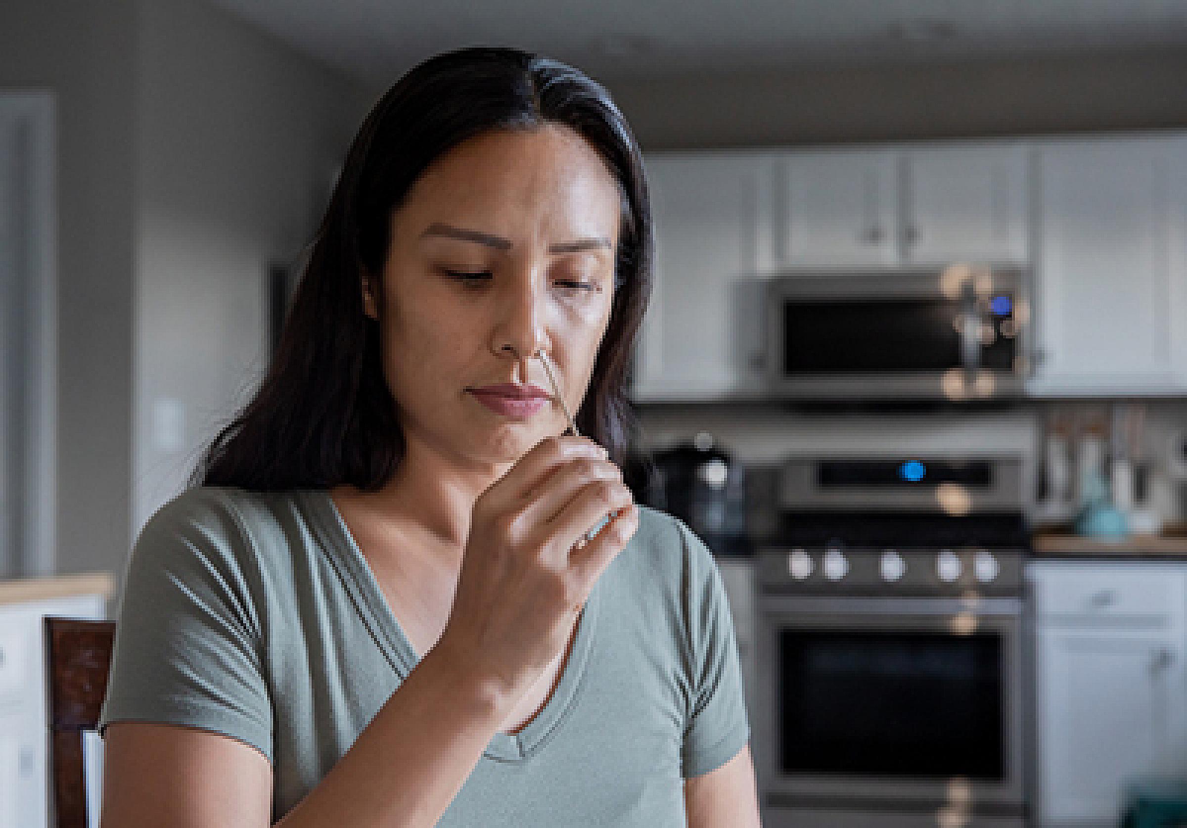 Woman standing in her kitchen and inserting a long cotton swab up her nose as part of a COVID-19 test