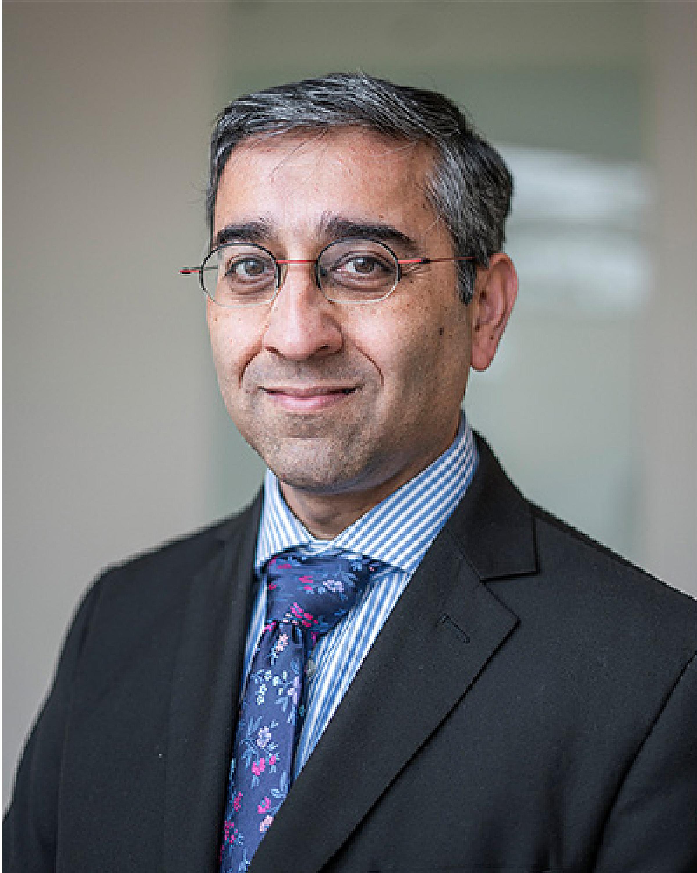 Manish Kohli wearing black suit and blue floral tie
