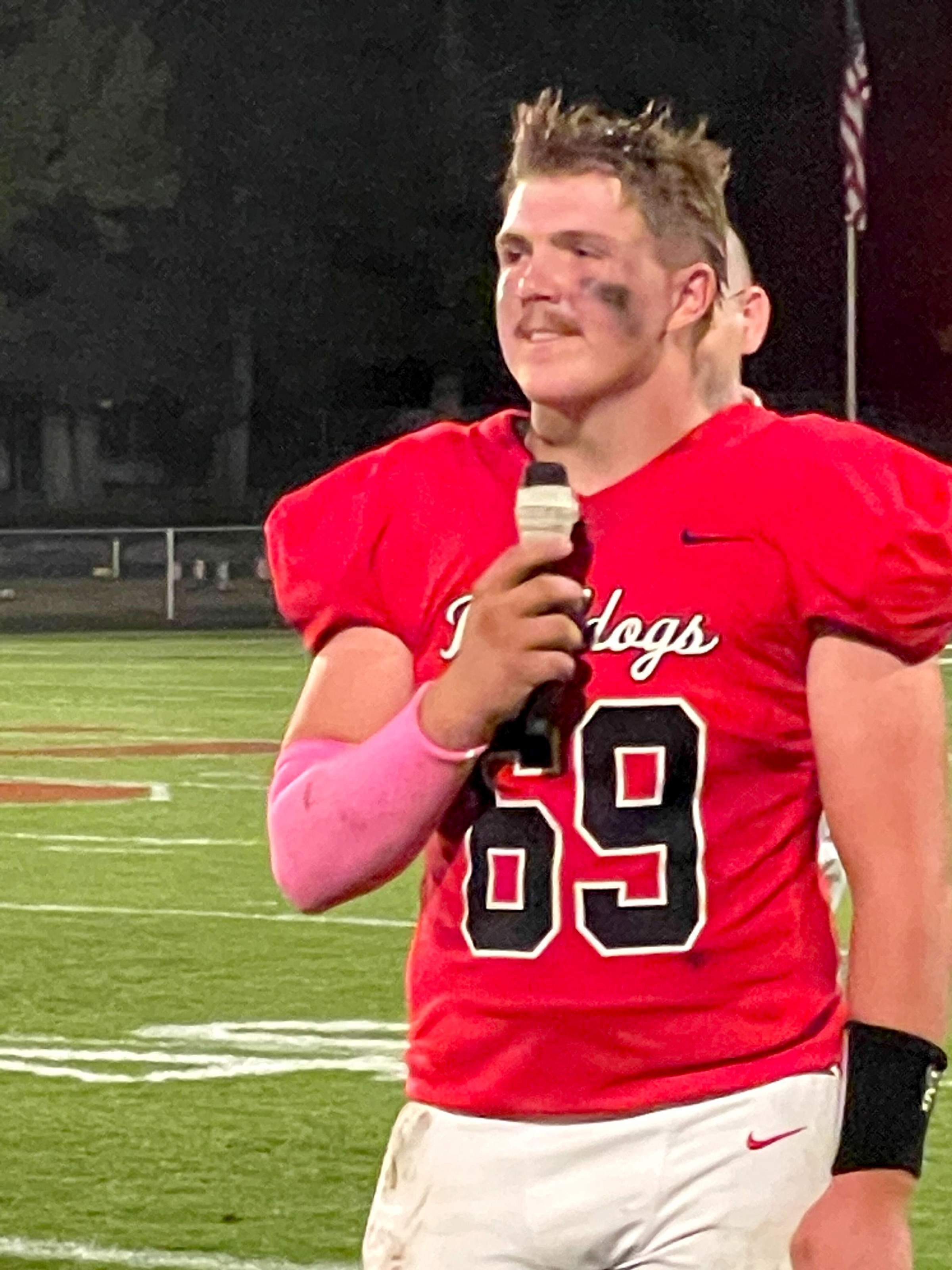 Gunner Stringham wearing his football gear and speaking into a microphone after his senior night football game