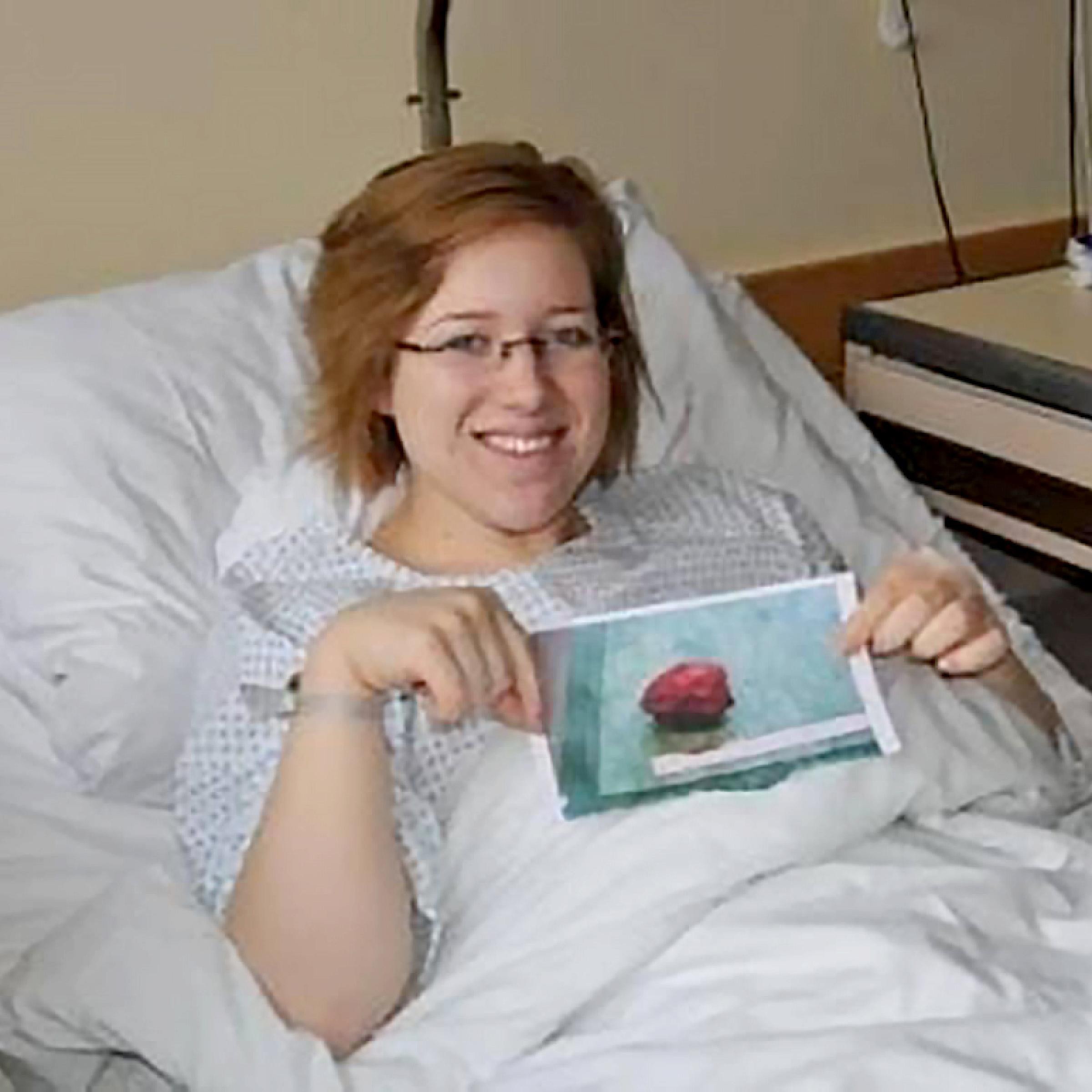 Emily Olsen in a hospital bed holding a photo of the tumor she had removed
