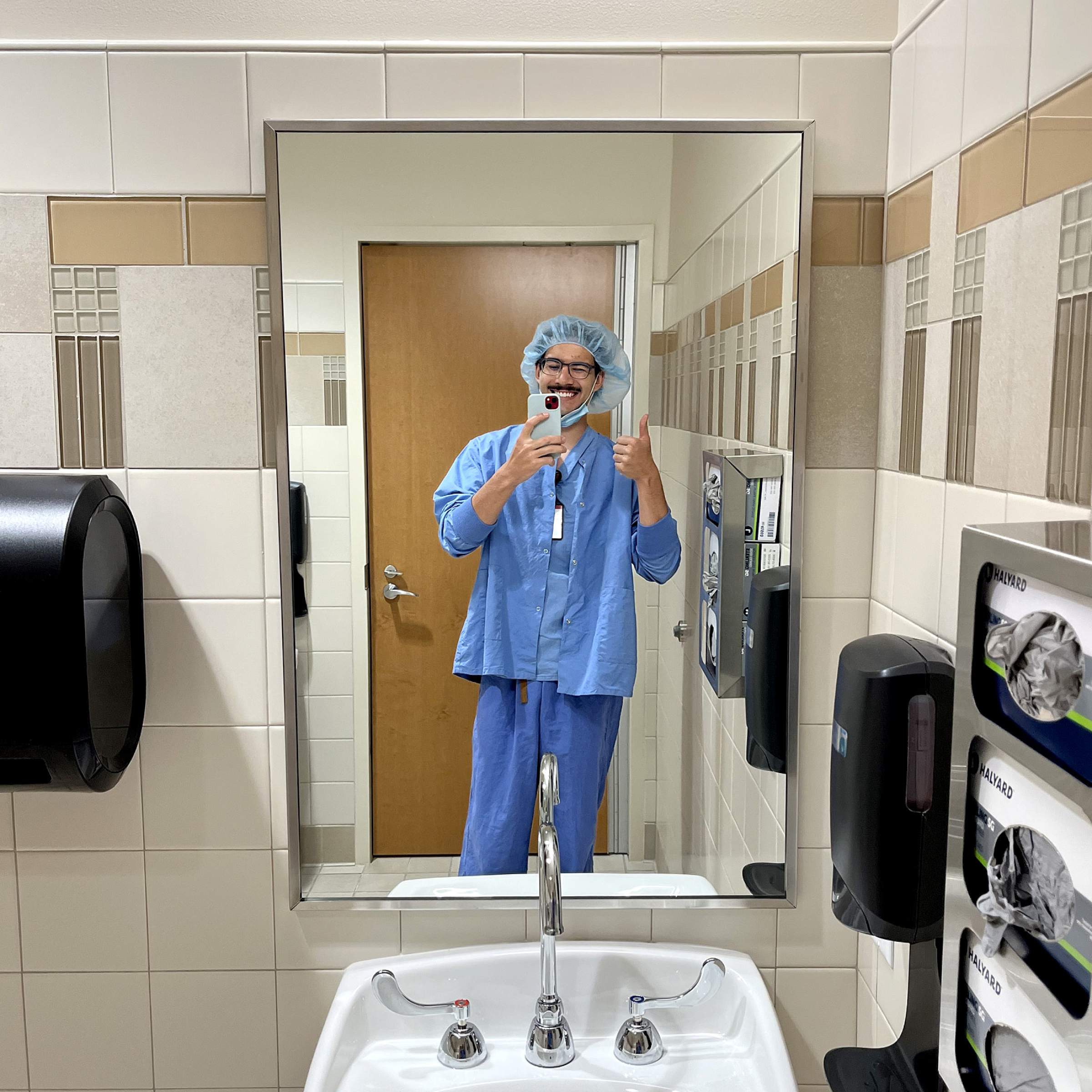 Anthony Bradley wearing scrubs and taking a picture of himself in a hospital bathroom mirror