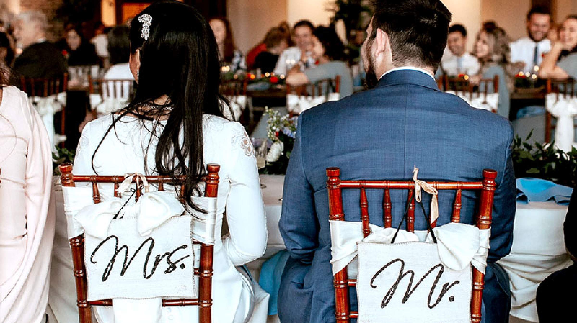 Bride and groom sit in chairs labeled Mr. and Mrs. at a wedding reception