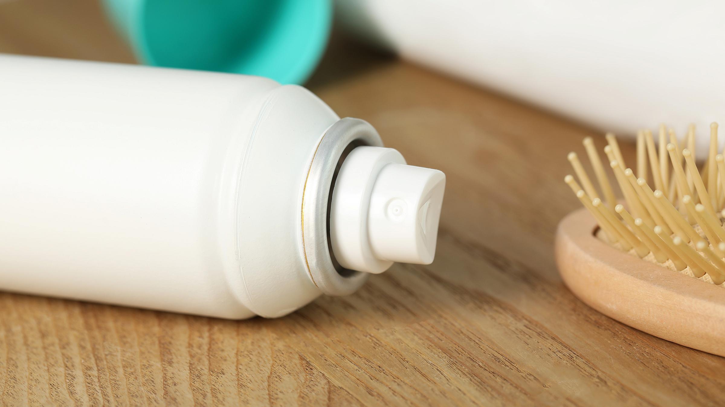 White aerosol spray bottle on its side next to a hair brush