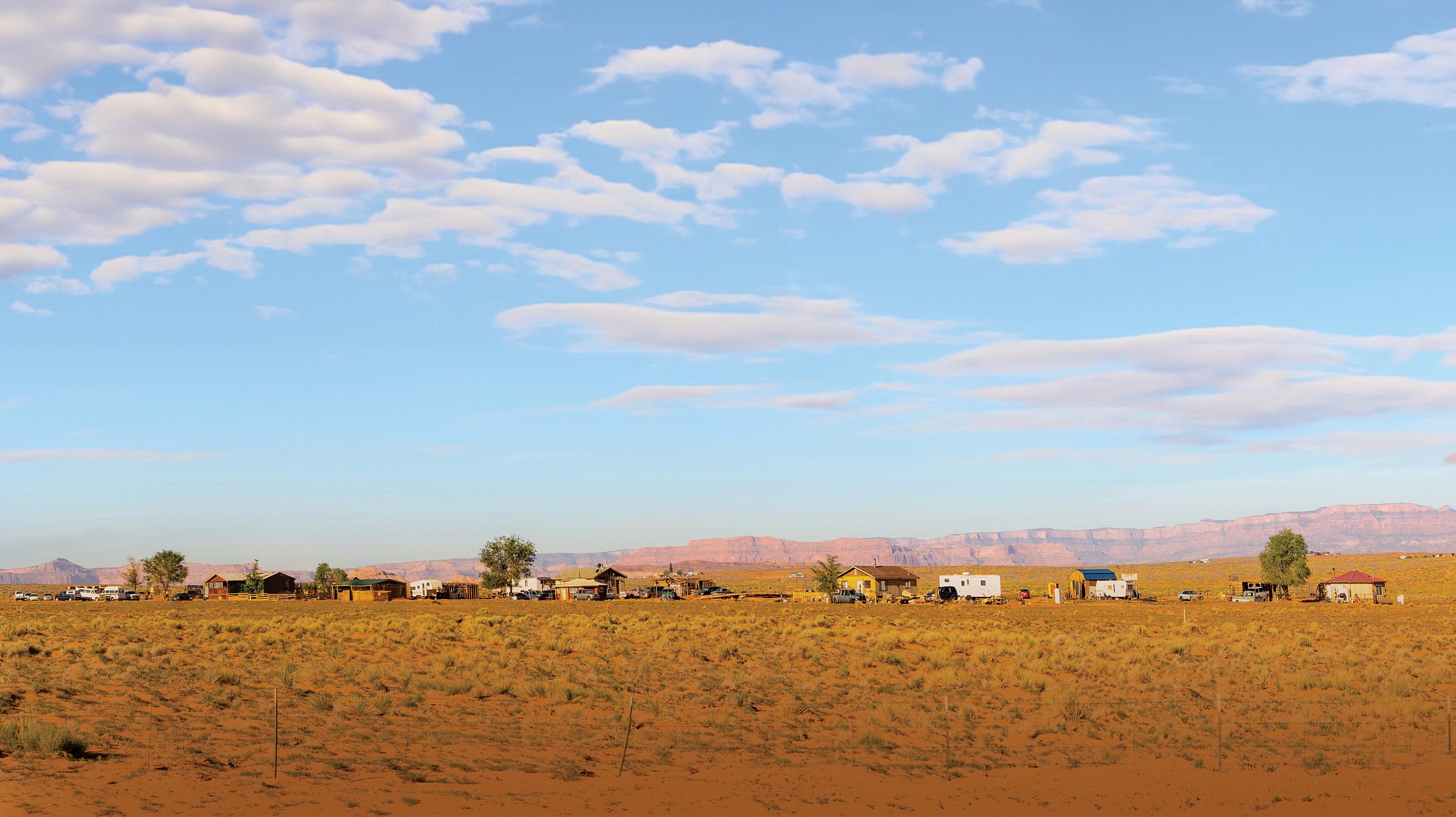 Distant buildings in a field of brown grass with clouds overhead