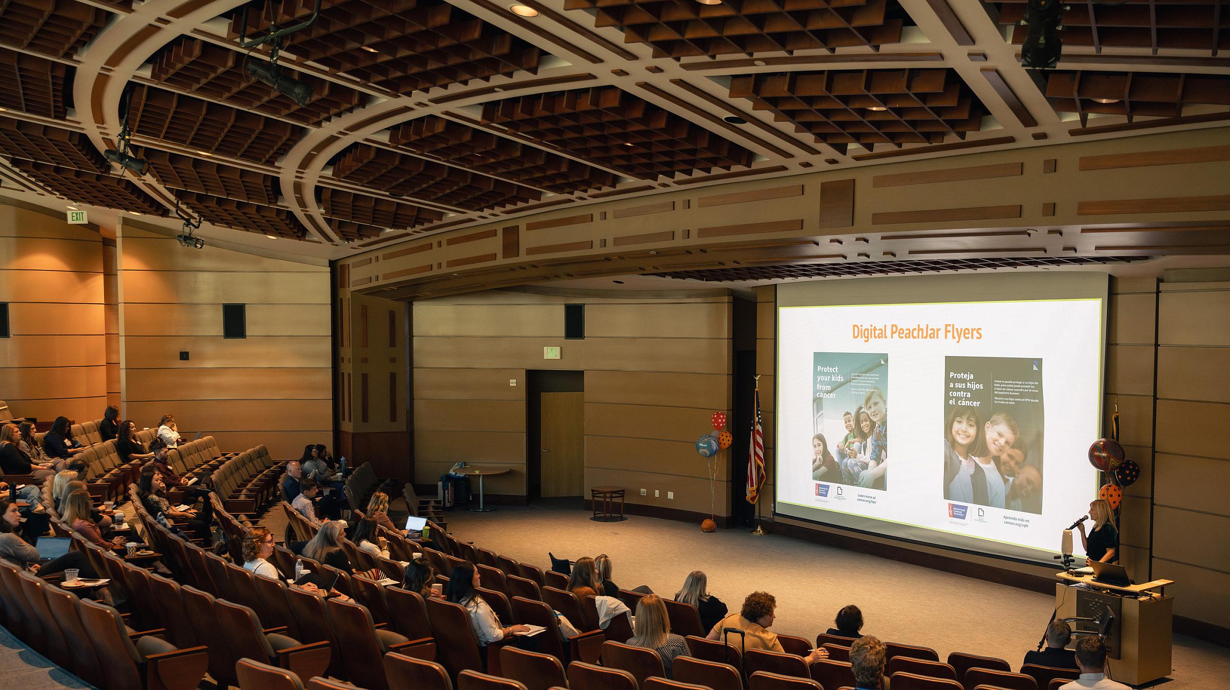 Speaker presents to audience in an auditorium with slide “Digital PeachJar Flyers” on projector.