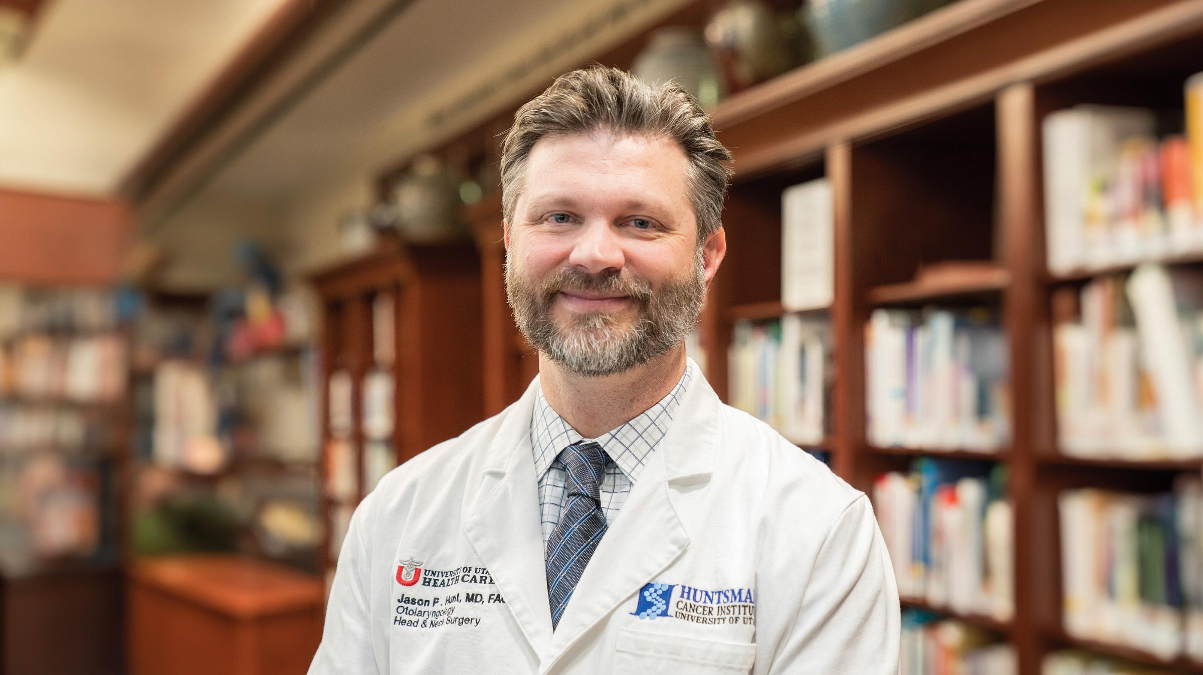 Jason Hunt wearing lab coat and posing next to bookshelves