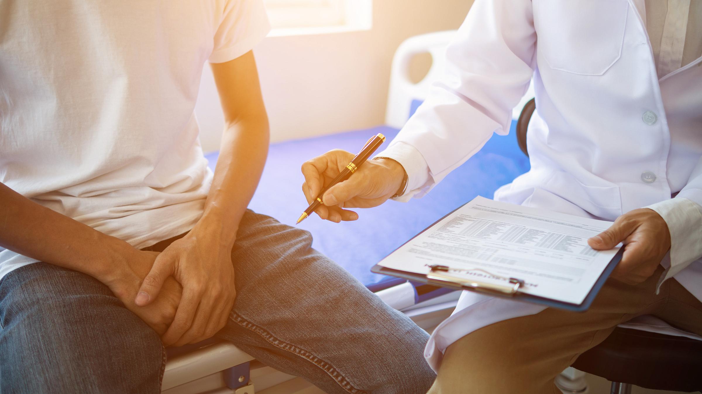 Doctor holding a clipboard and gesturing with a pen while sitting next to patient