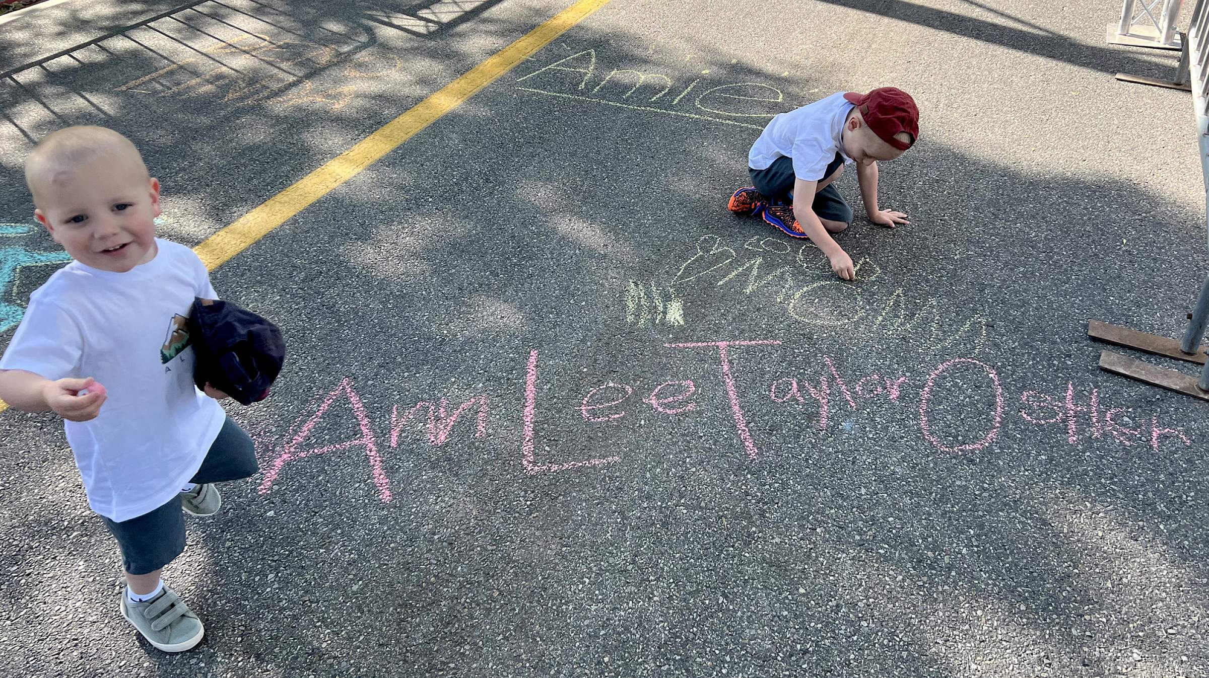 Steve and Ann Ostler's kids draw on pavement with chalk; "Ann Lee Taylor Ostler" is written on the pavement in front of them