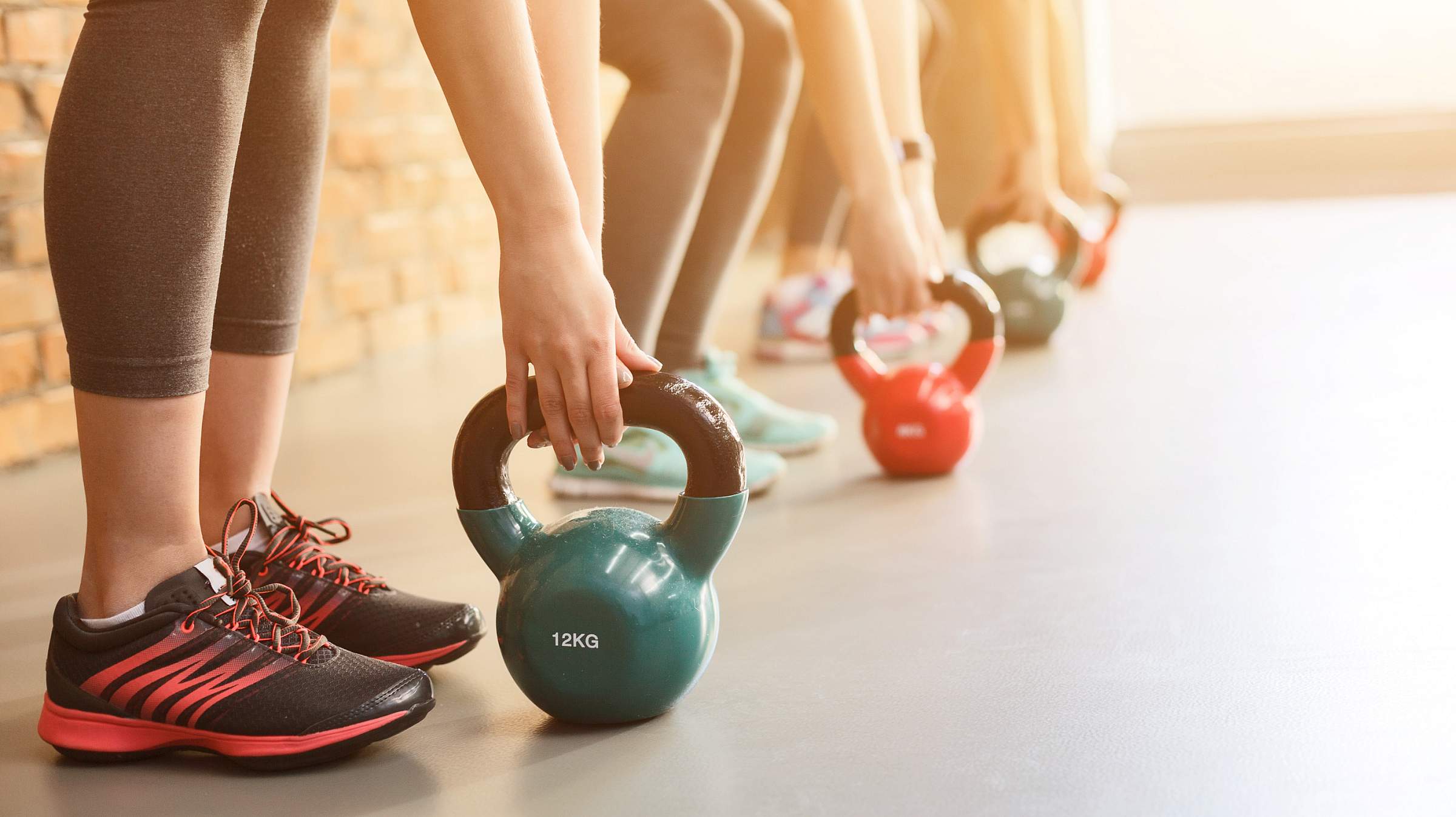 Row of people leaning down to pick up kettlebell weights