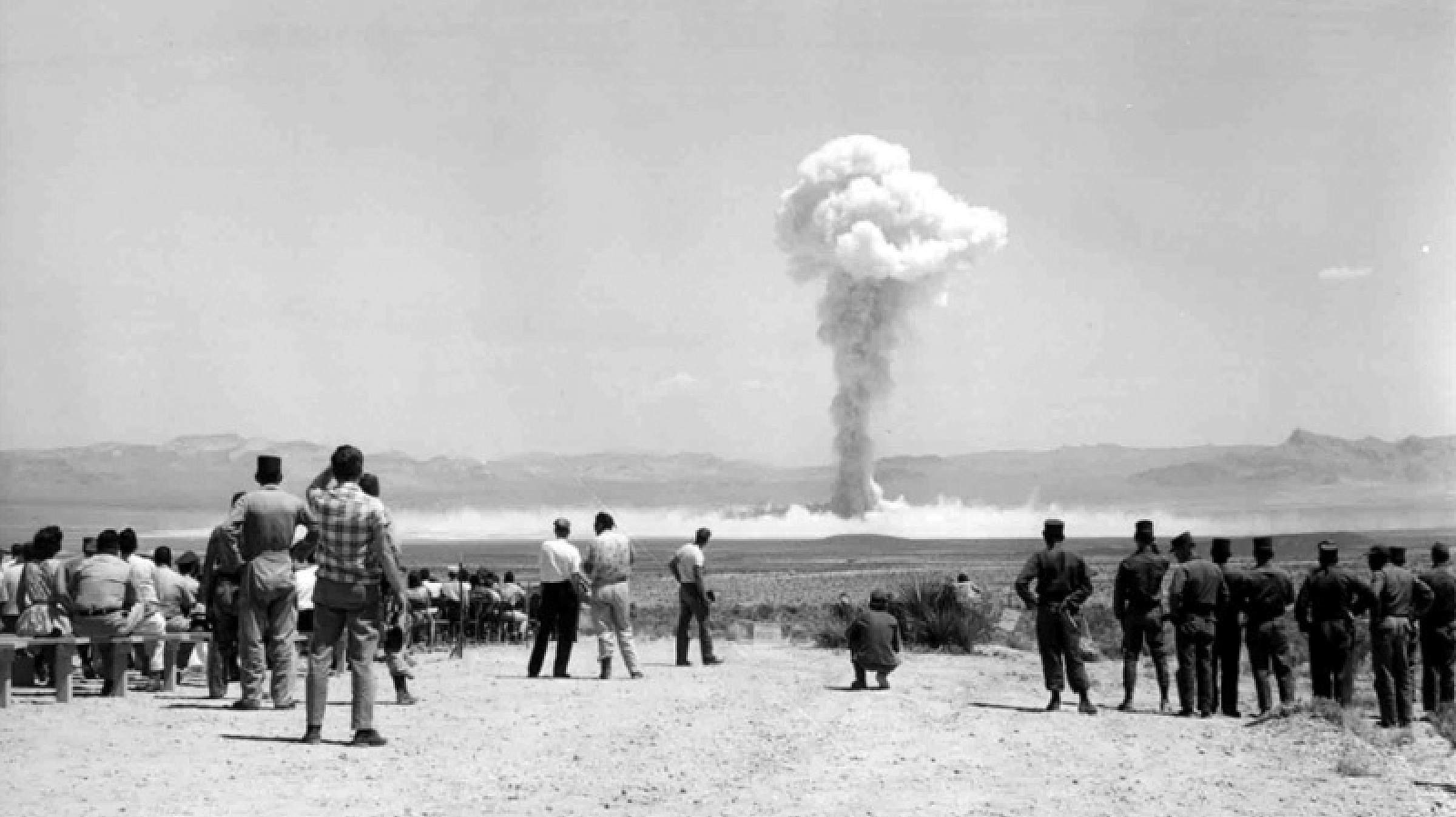 Historic photo of a nuclear test at the Nevada test site with people watching.