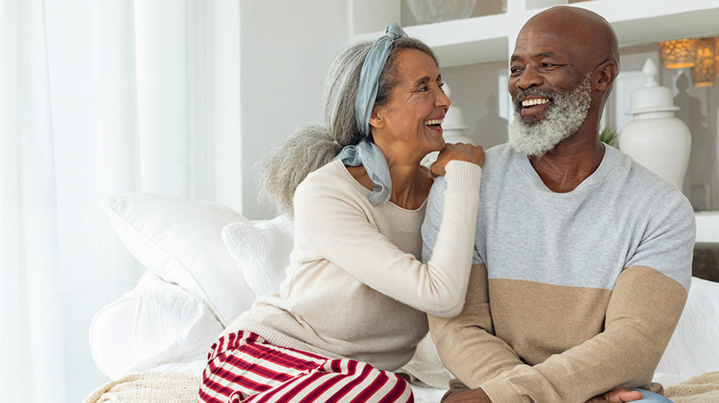 Man and Woman Sitting on Bed at Home Together Smiling