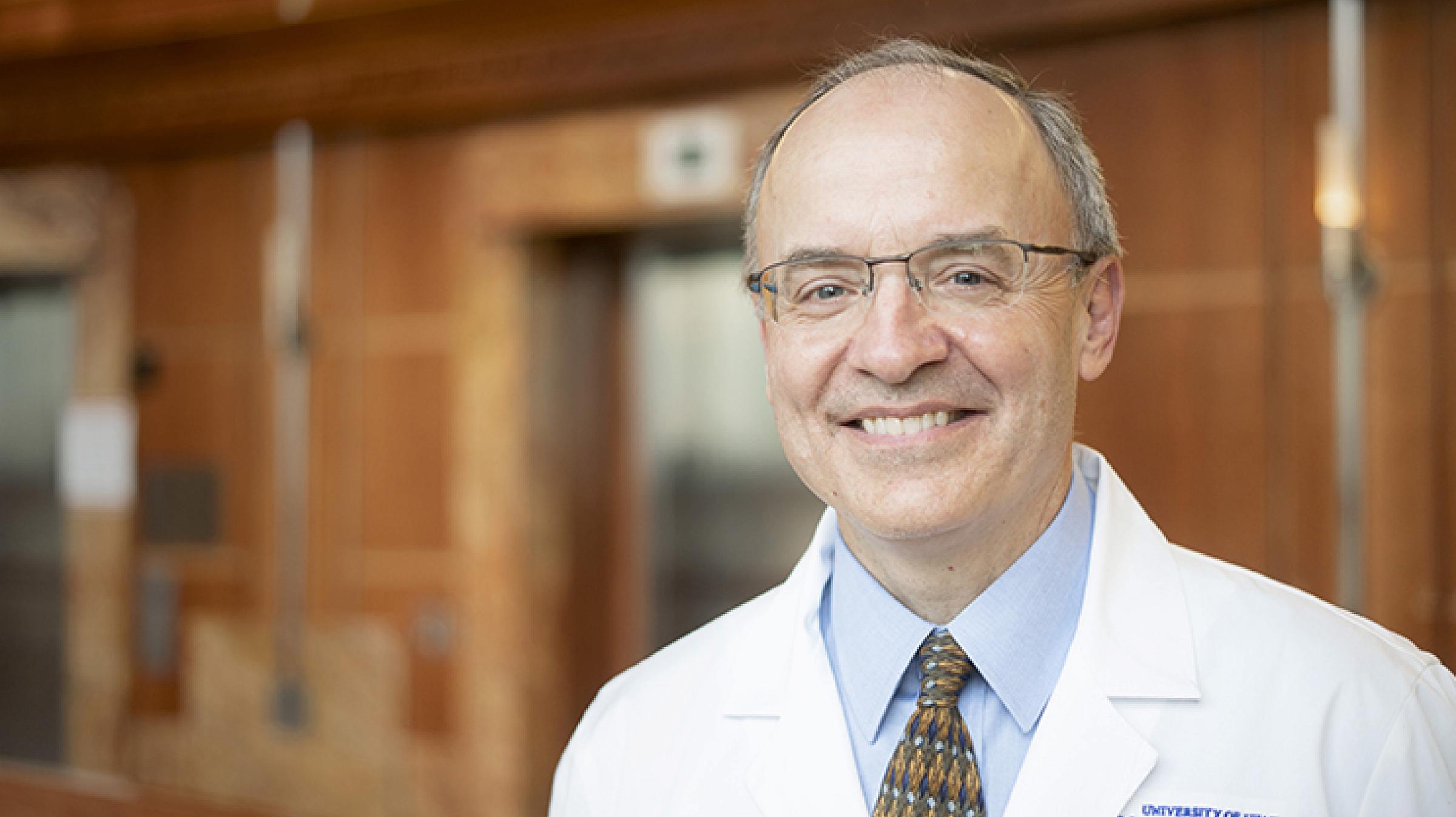 White man, Michael Pulsipher, MD, smiling wearing a white lab coat in front of elevators