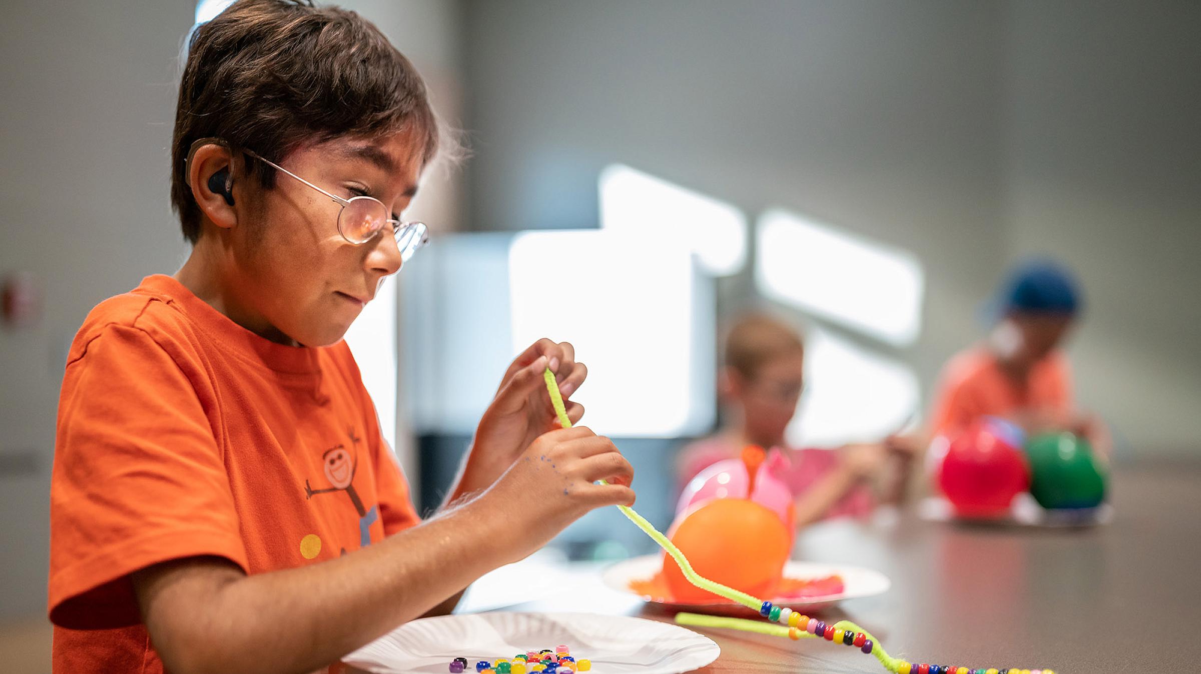 Ten-year-old Gabe concentrates on stringing beads to create legs for his bug.