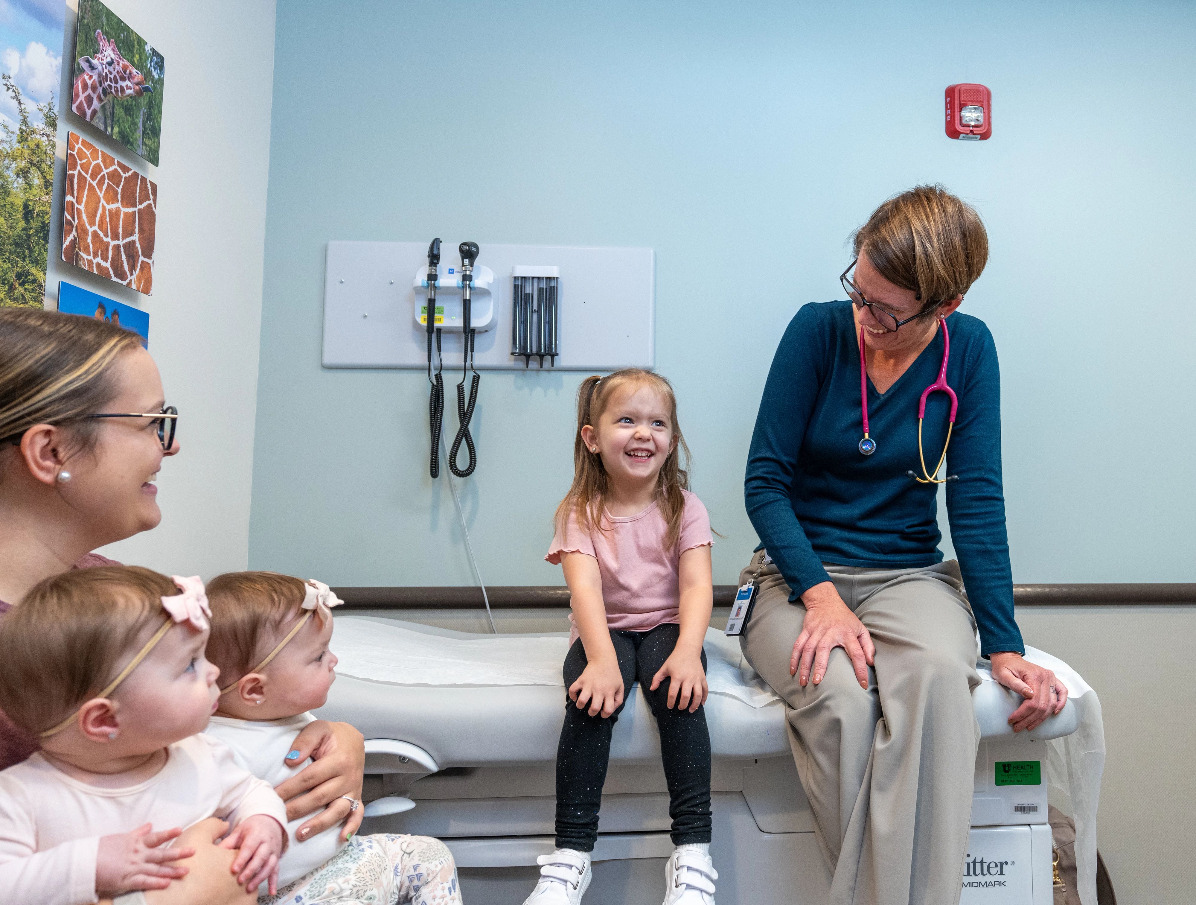 A girl sitting next to her pediatrician while her mom watches