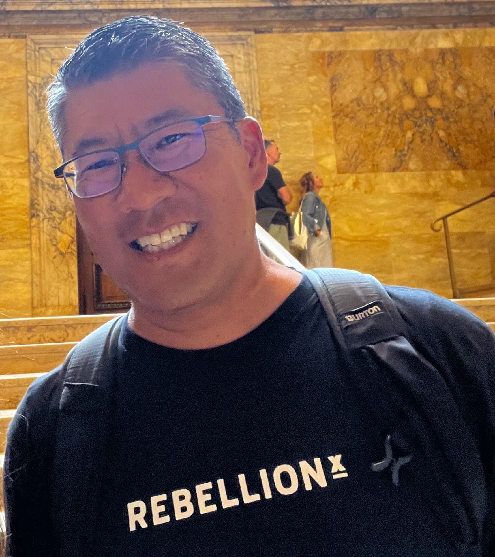 Doug Akagi in a black shirt and backpack smiling