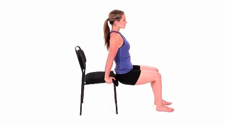 Person holding on to a chair in a squatting position getting ready to perform a chair dip exercise.