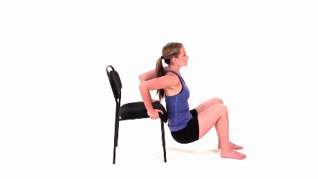 Person holding on to a chair while squatting down to the floor performing a chair dip exercise.