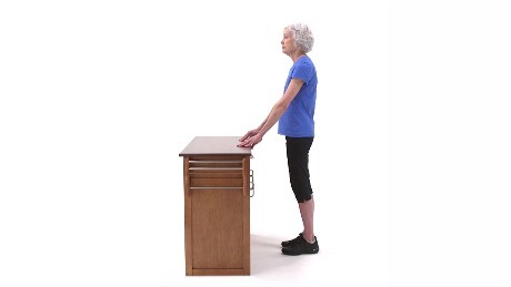 Person standing at a desk with hands placed on getting ready to perform a hip extension exercise