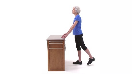 Person standing at a desk with their left leg outstretched behind them performing a hip extension