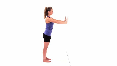 Person standing at a wall with their hands on the wall getting ready to perform a wall pushup.