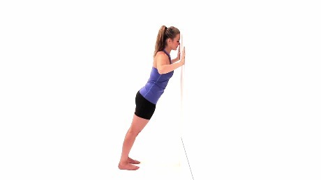Person pushed up against a wall, performing a wall pushup.