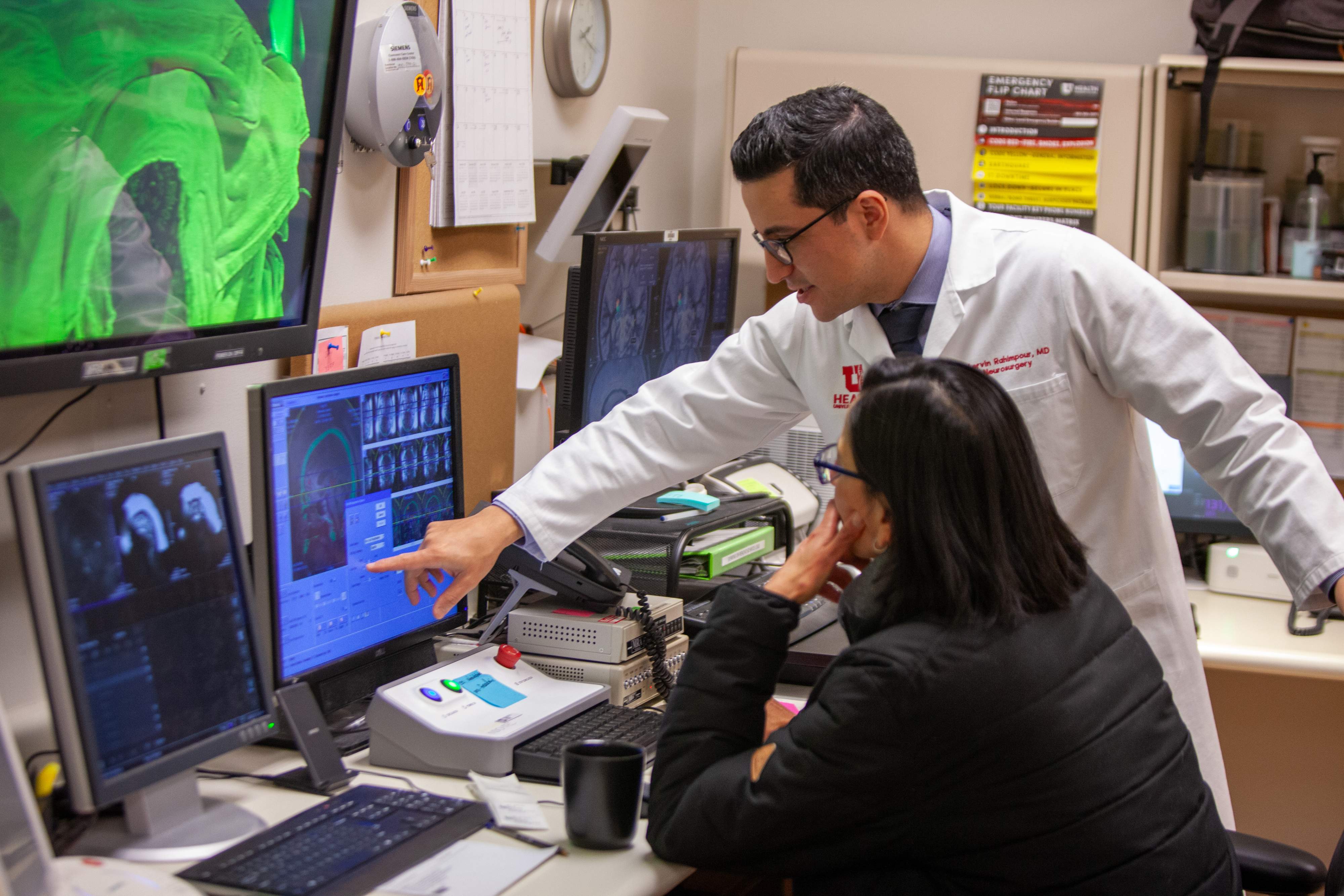 Dr. Shervin Rahimpour and Dr. Lubdha Shah look at MRI scans of patient's brain during focused ultrasound procedure.