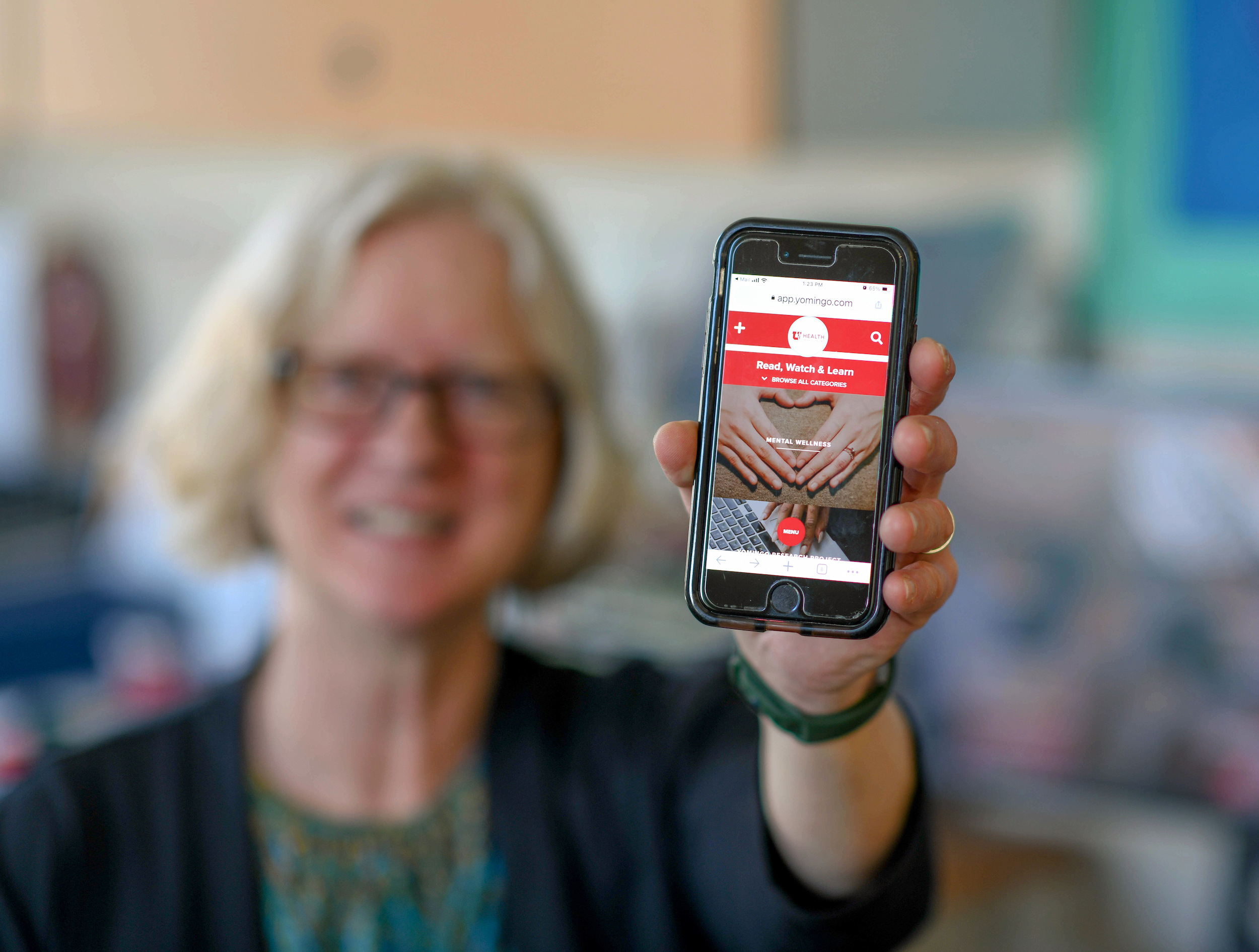 Blurry photo of a person holding up a phone to the camera. The phone screen displays a maternal mental health app.