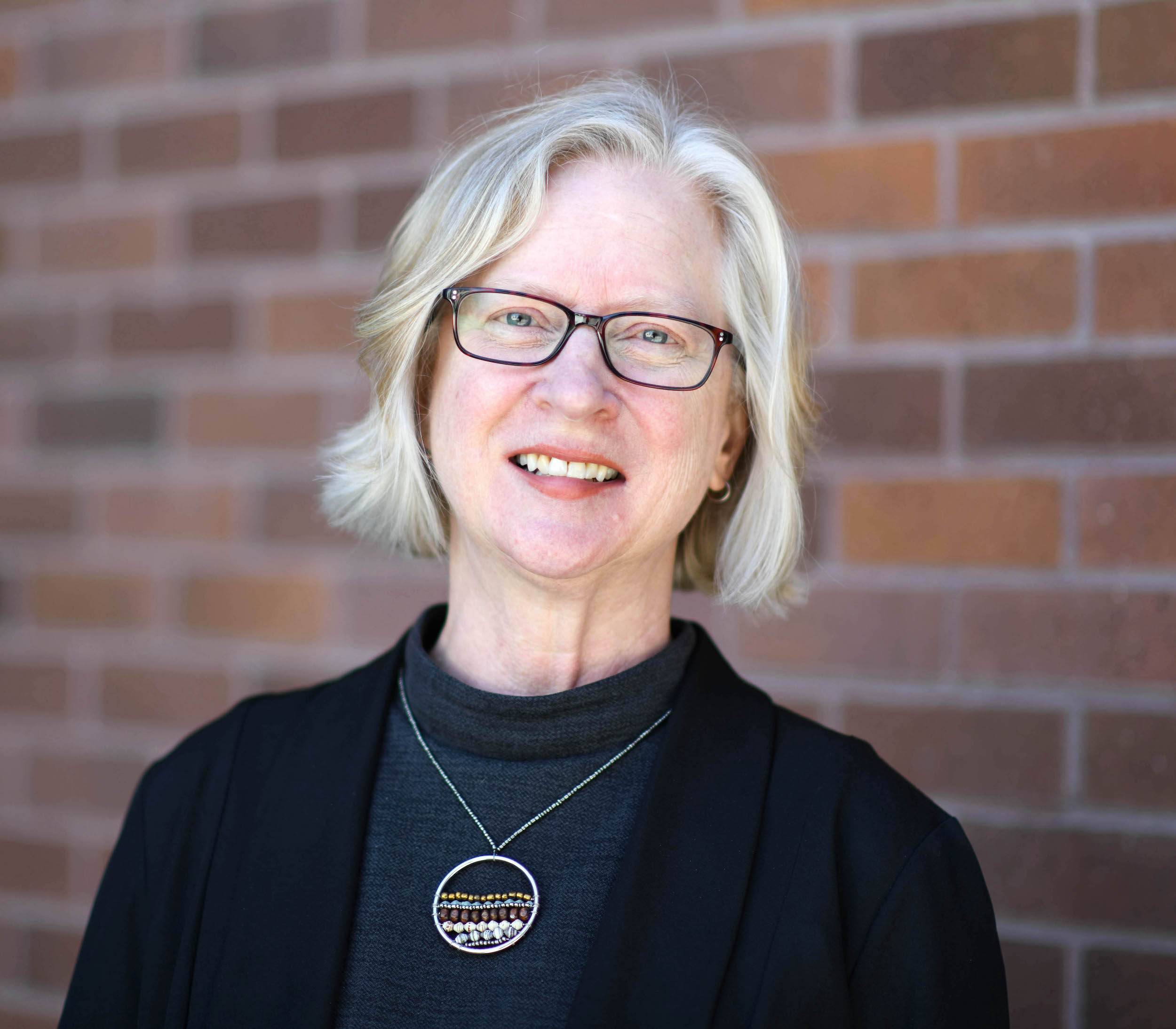 A person in a black blazer smiles at the camera.