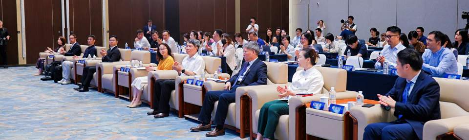 Photo of a small but fancy seminar room full of a crowd of applauding, formally dressed people.