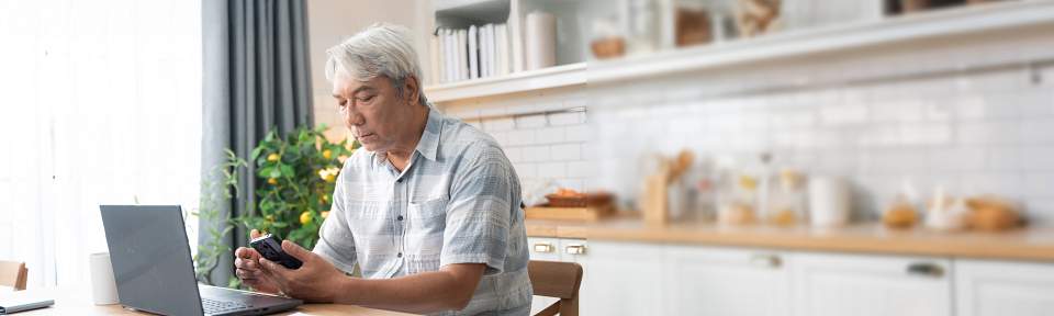 Senior man checking on mobile phone while working with laptop