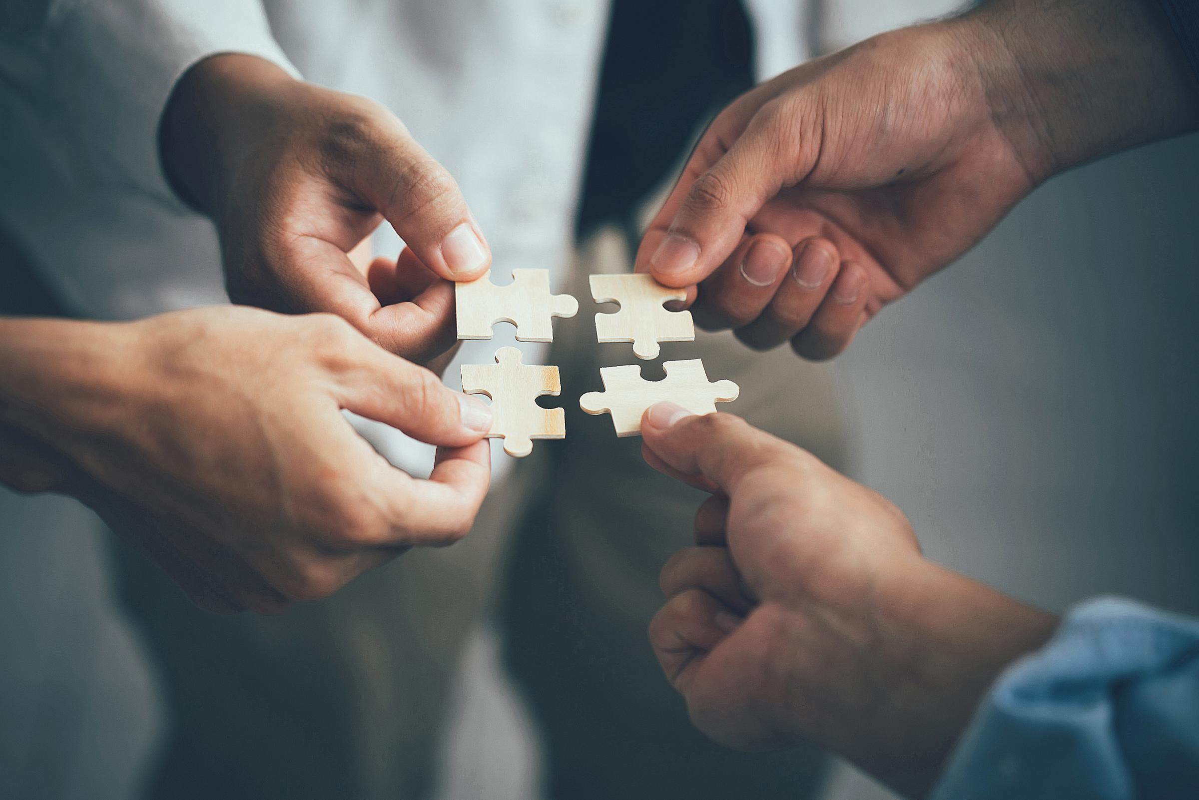 Four separate hands each hold puzzle pieces 