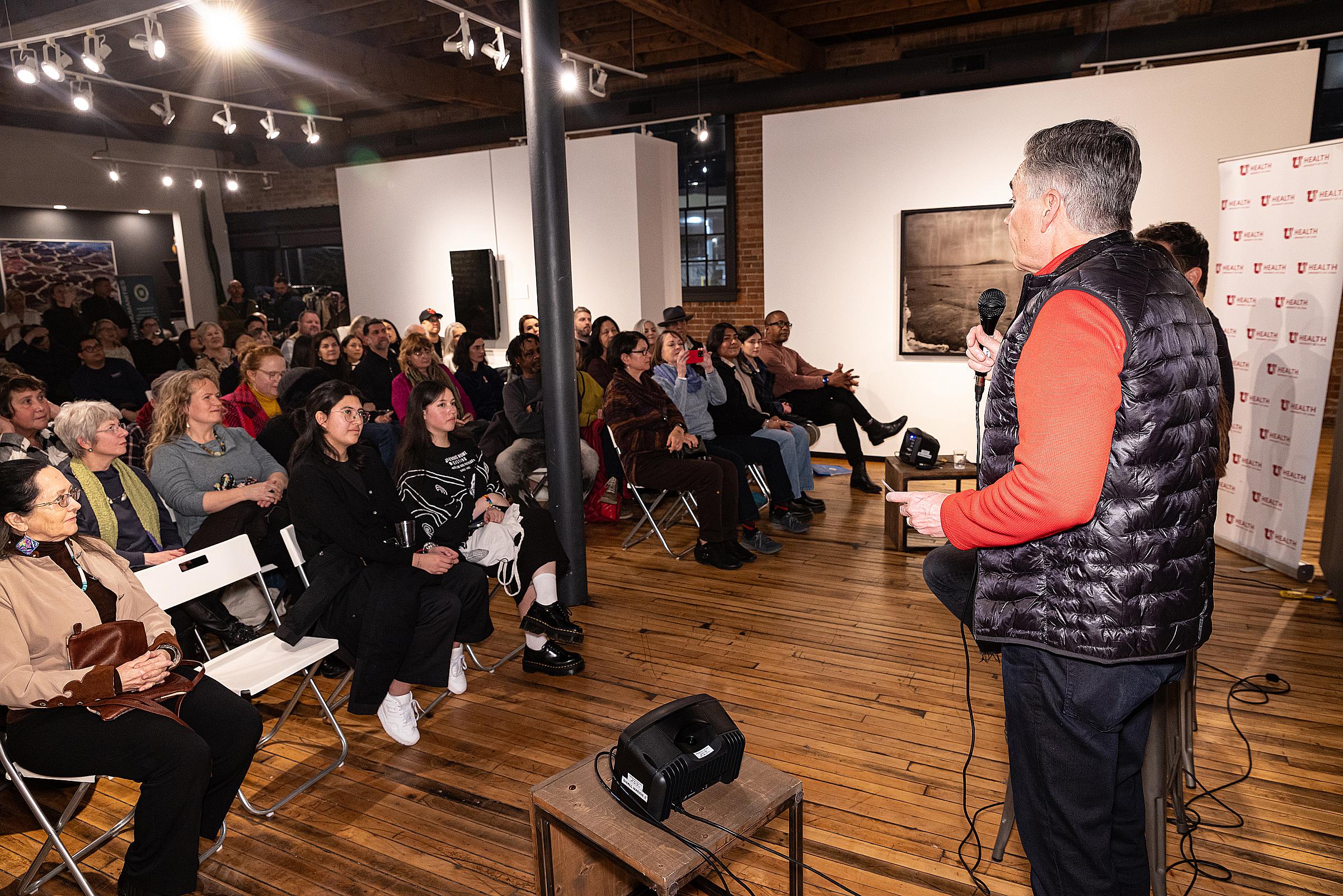 A man with a microphone speaks to a room full of people.