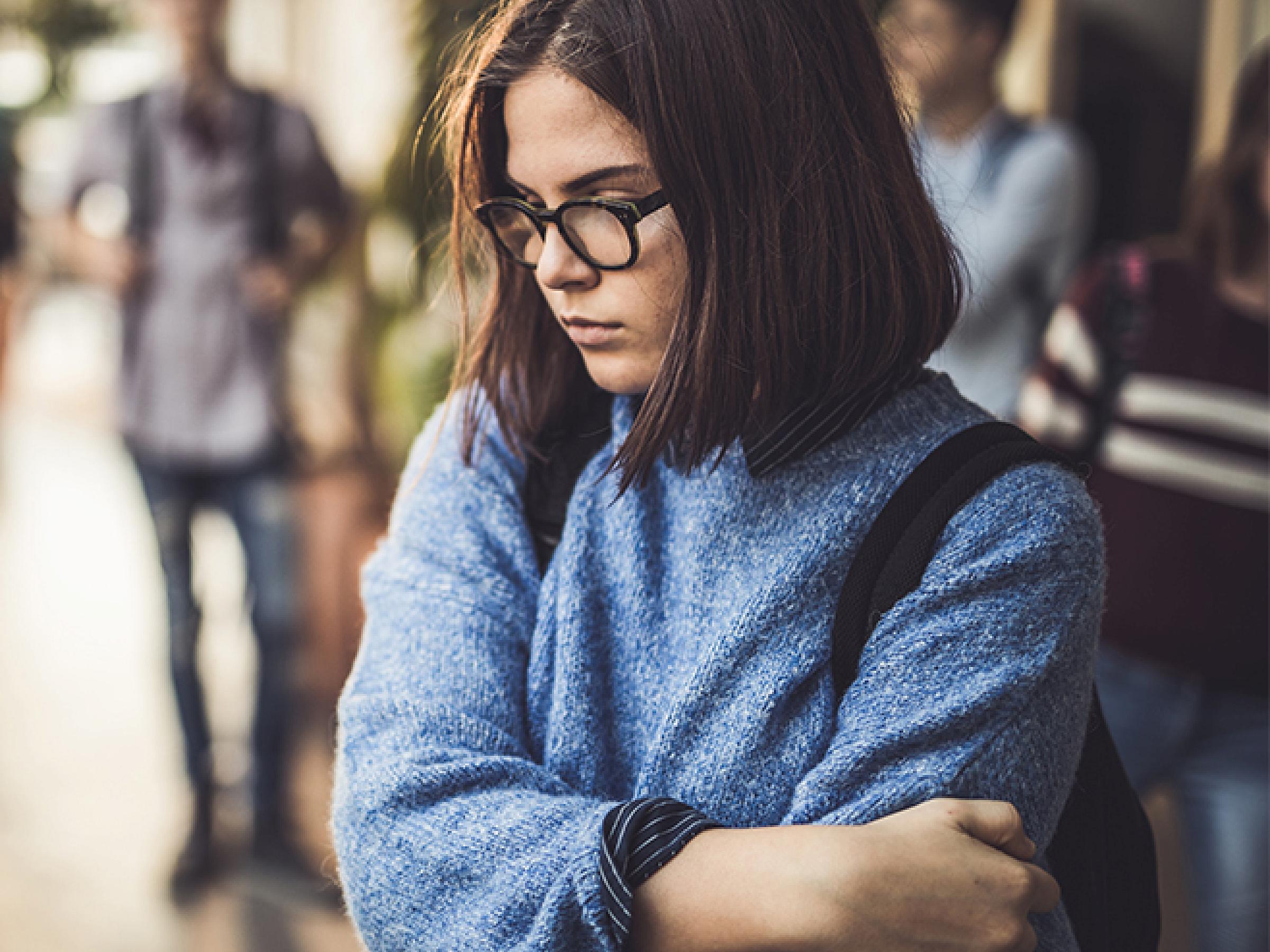 Young girl is sad and crosses her arms in the hallway at school