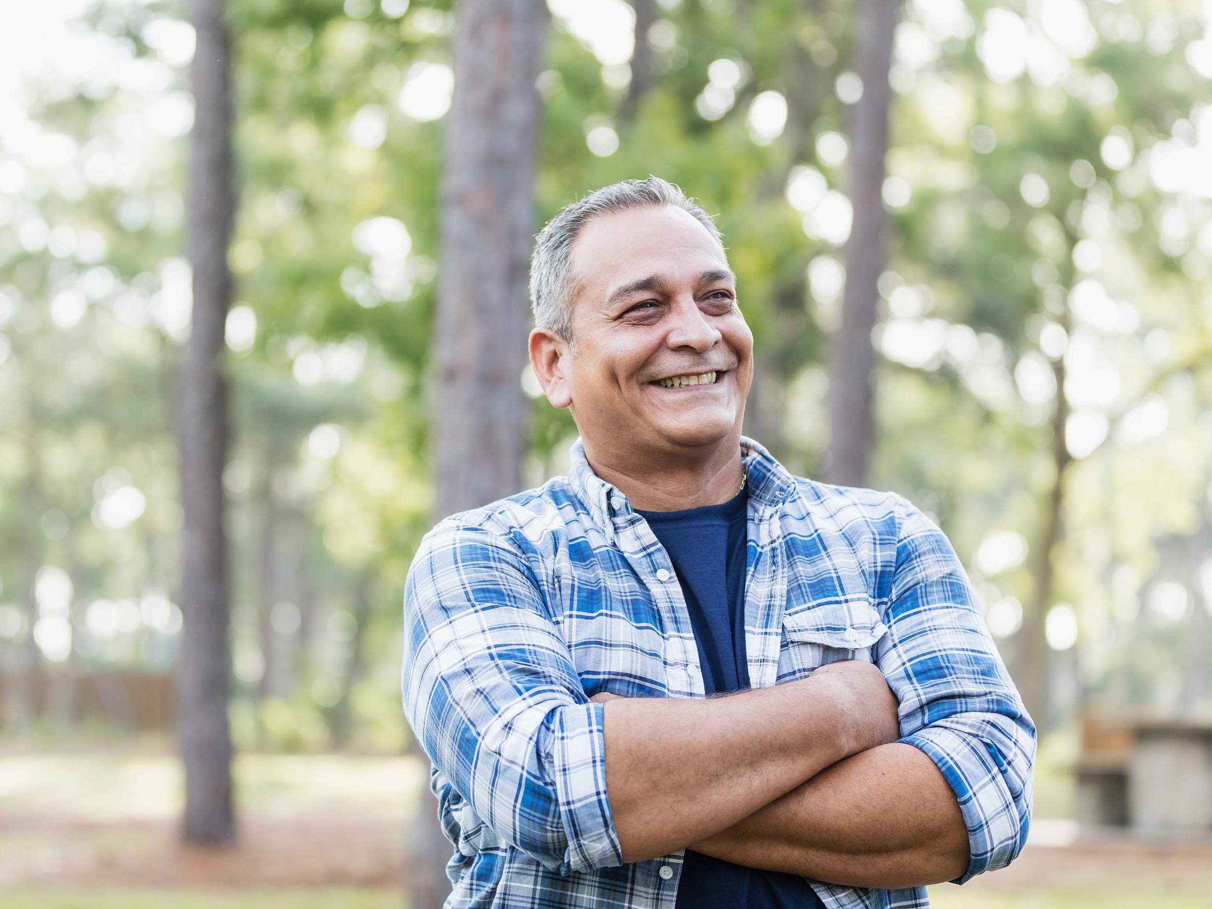 Older man with arms crossed smiling outside