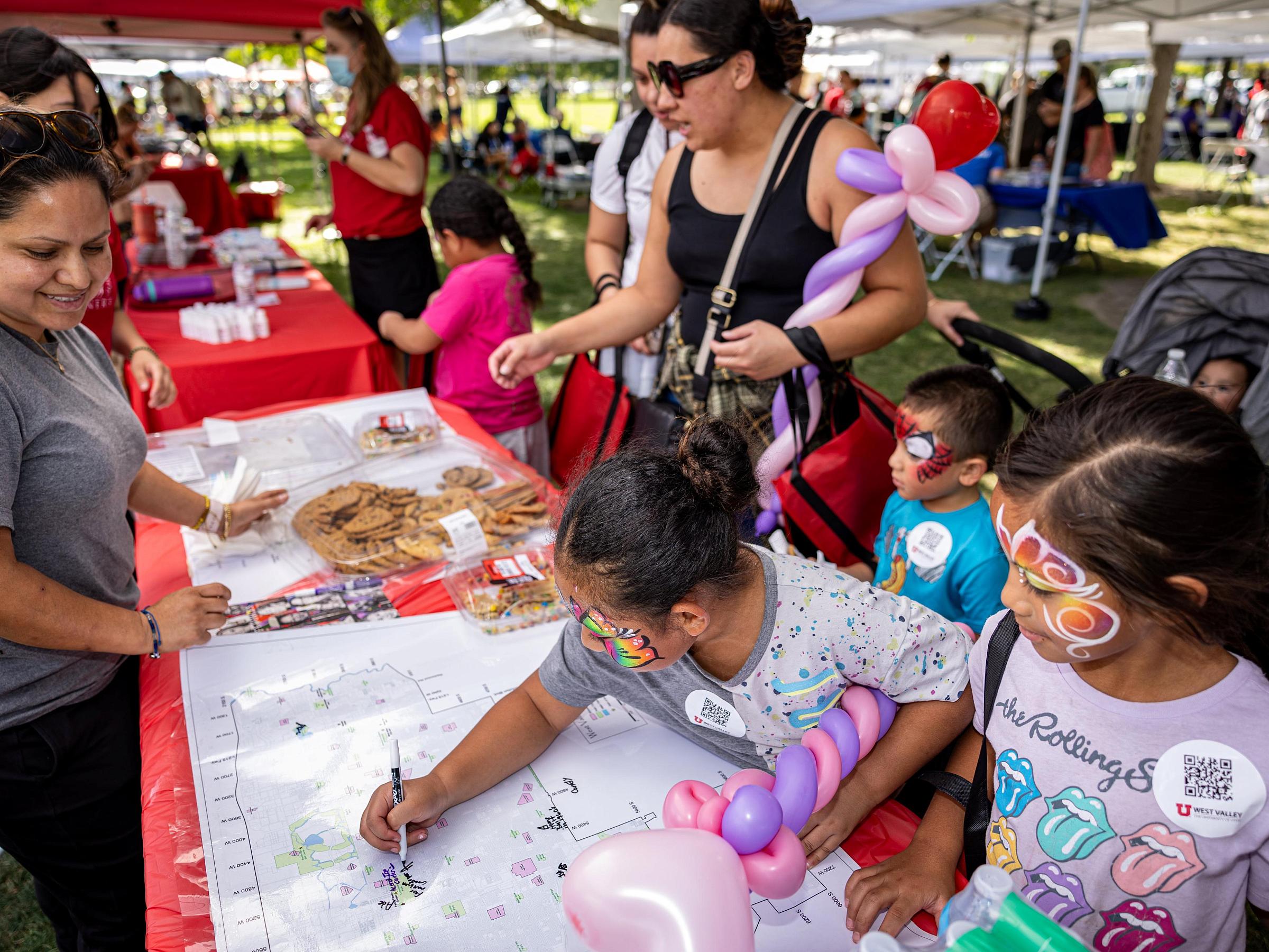 Young children with face paint draw at a booth