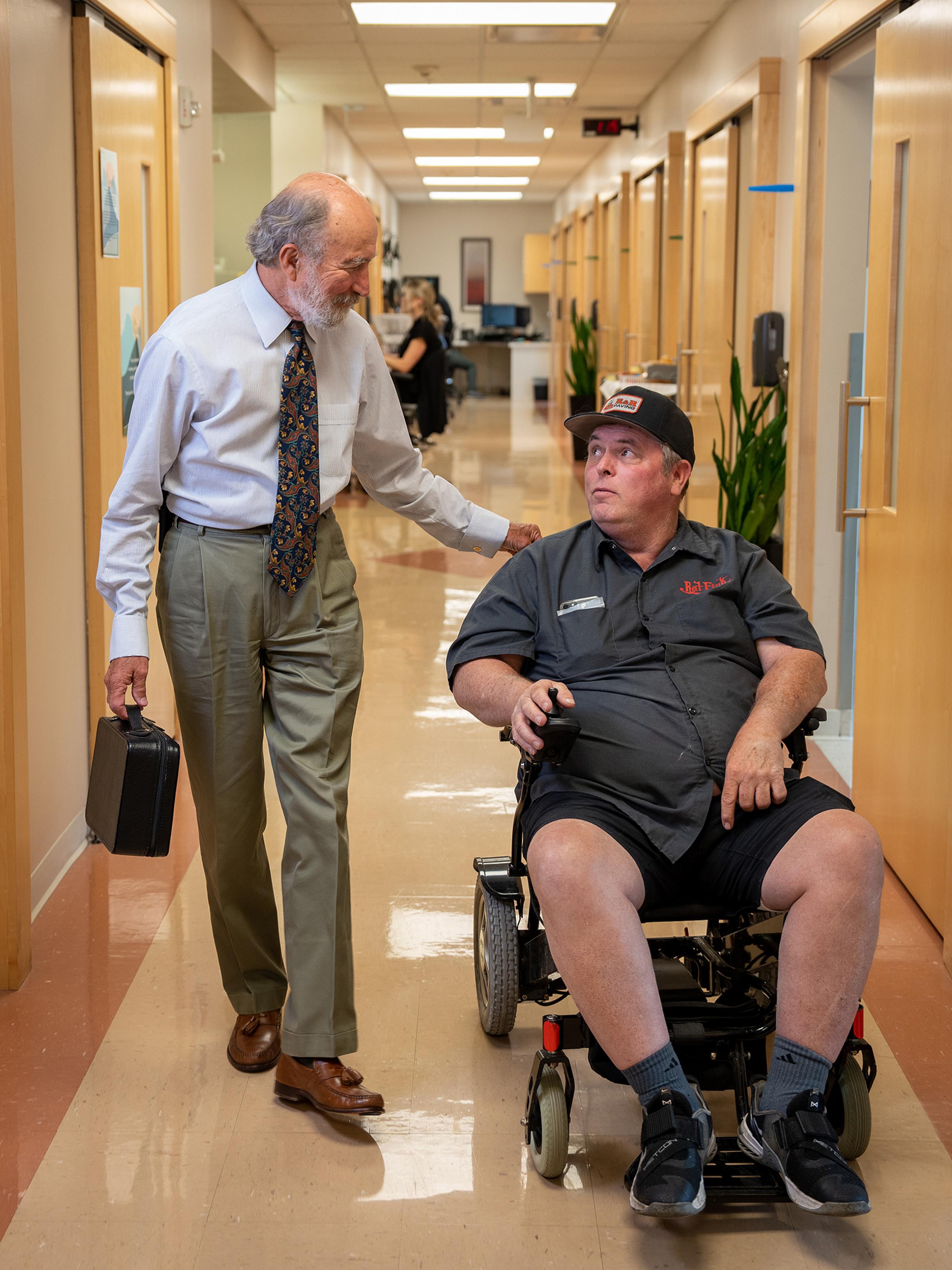 Dr. Bromberg, U of U Health neurologist, talks to older male patient in wheelchair in hallway.