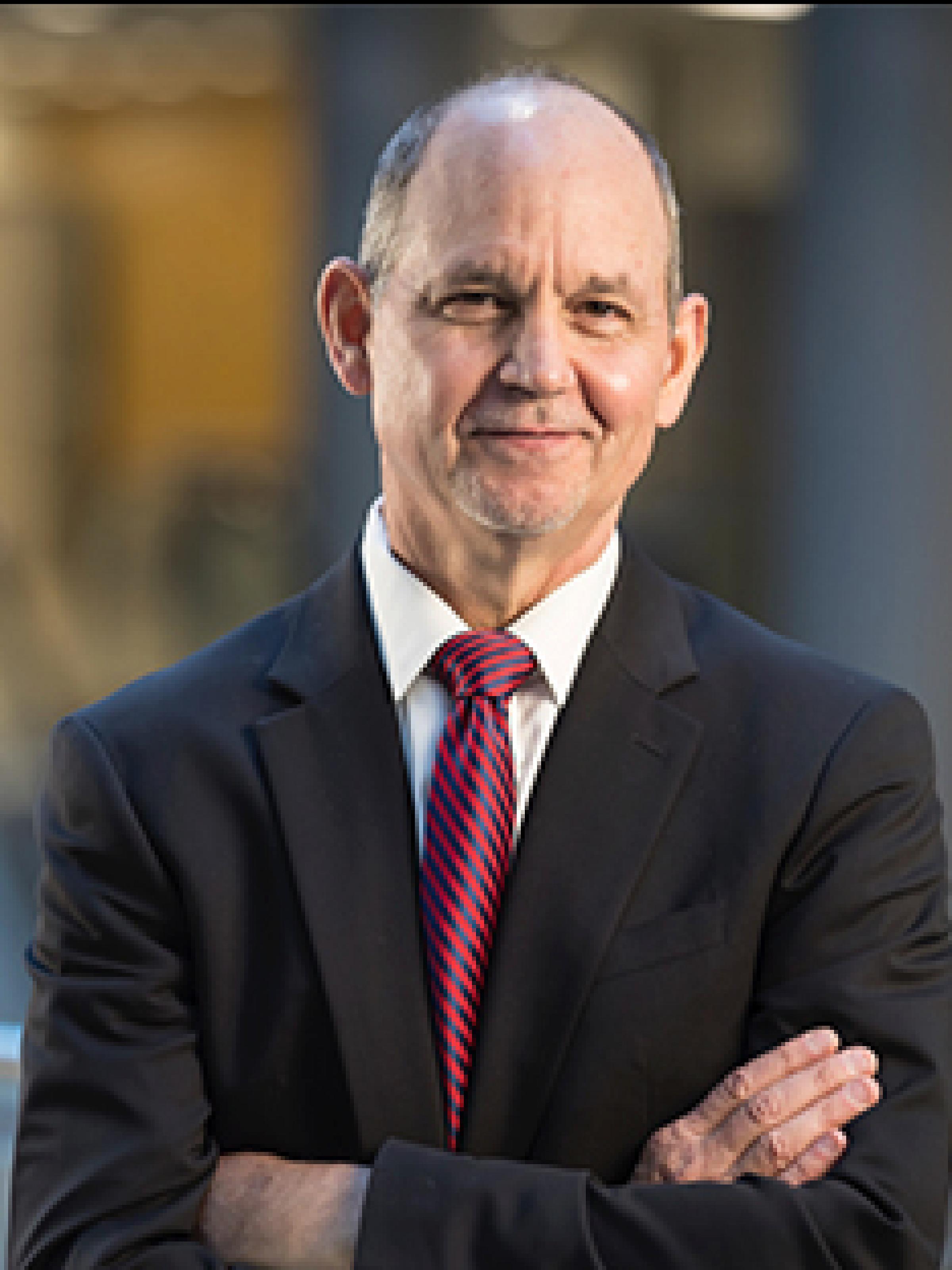 A white man wears a suit and tie and poses for a professional headshot