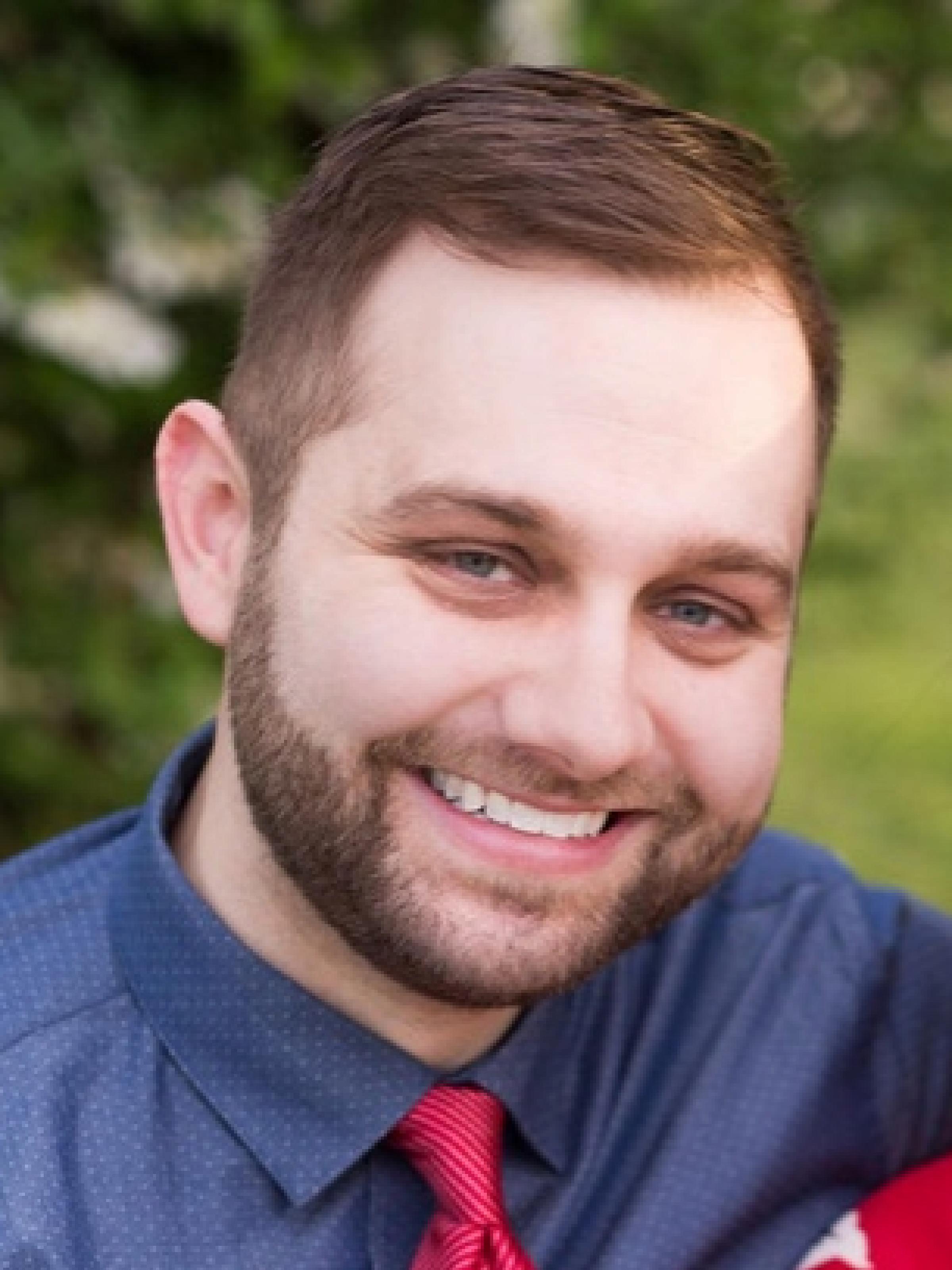 Man with brown hair and short brown beard smiles outside