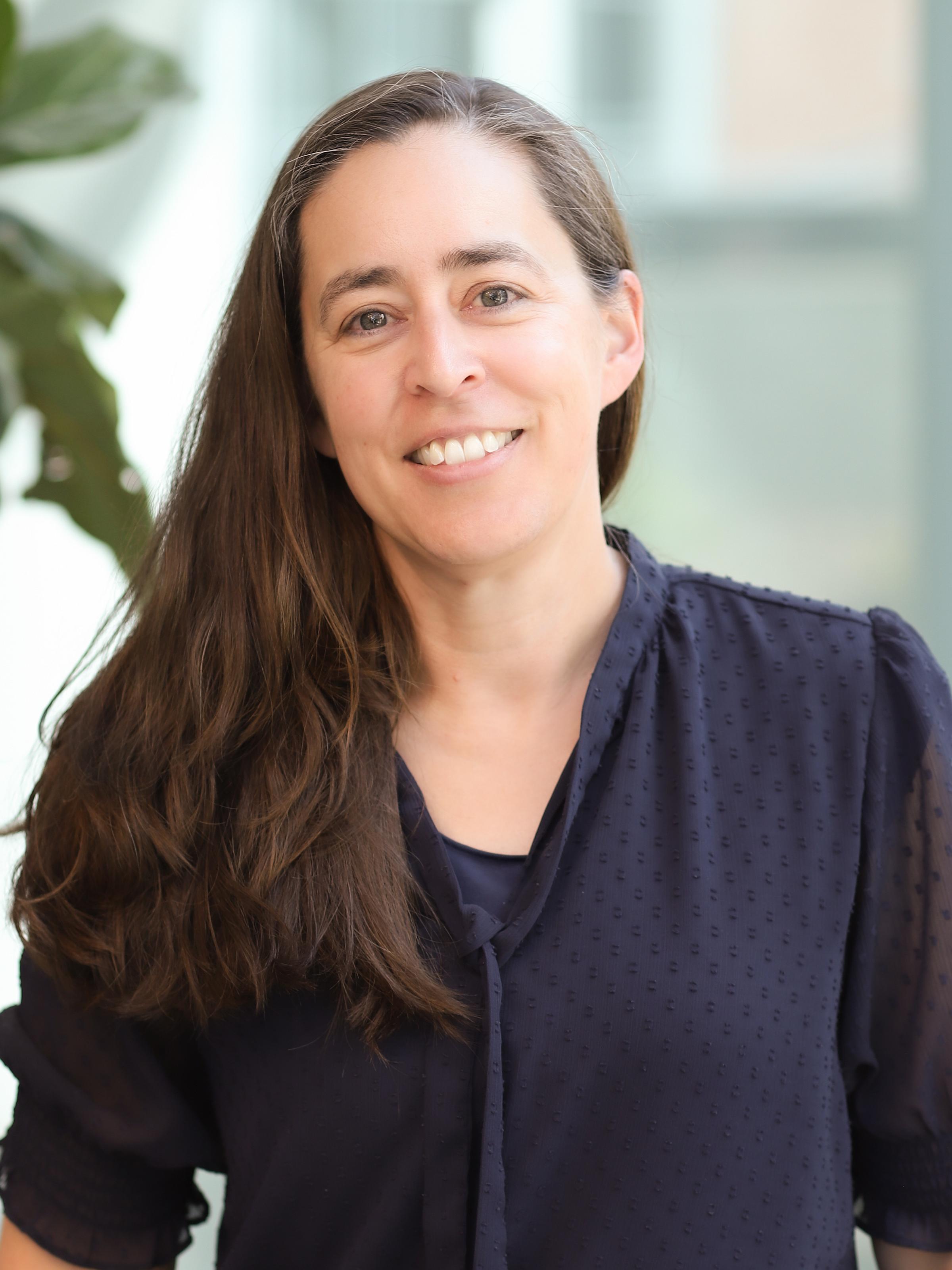 A person in a dark blouse smiling at the camera.