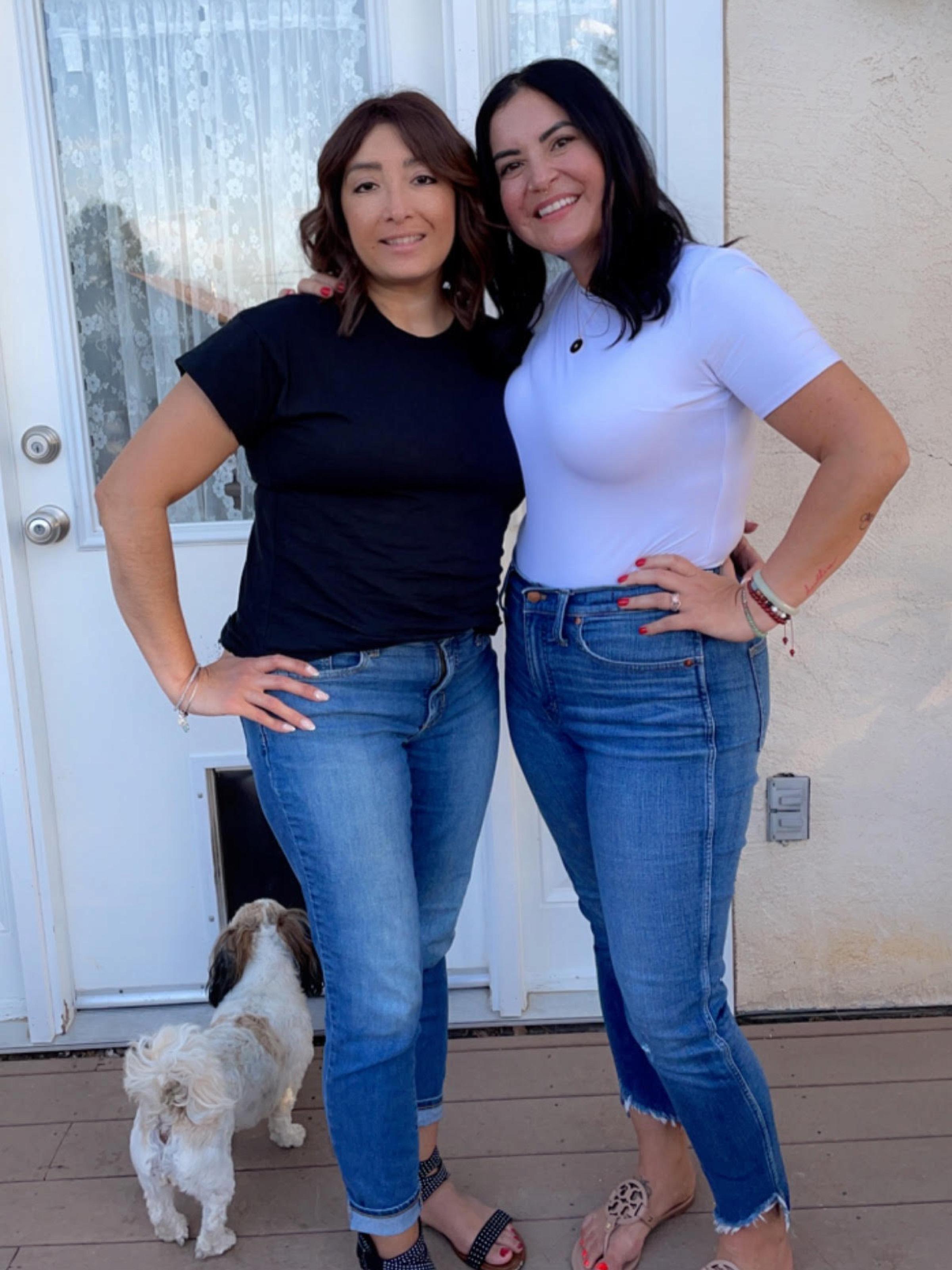 Two women who look similar pose, smile, and hug each other with one arm
