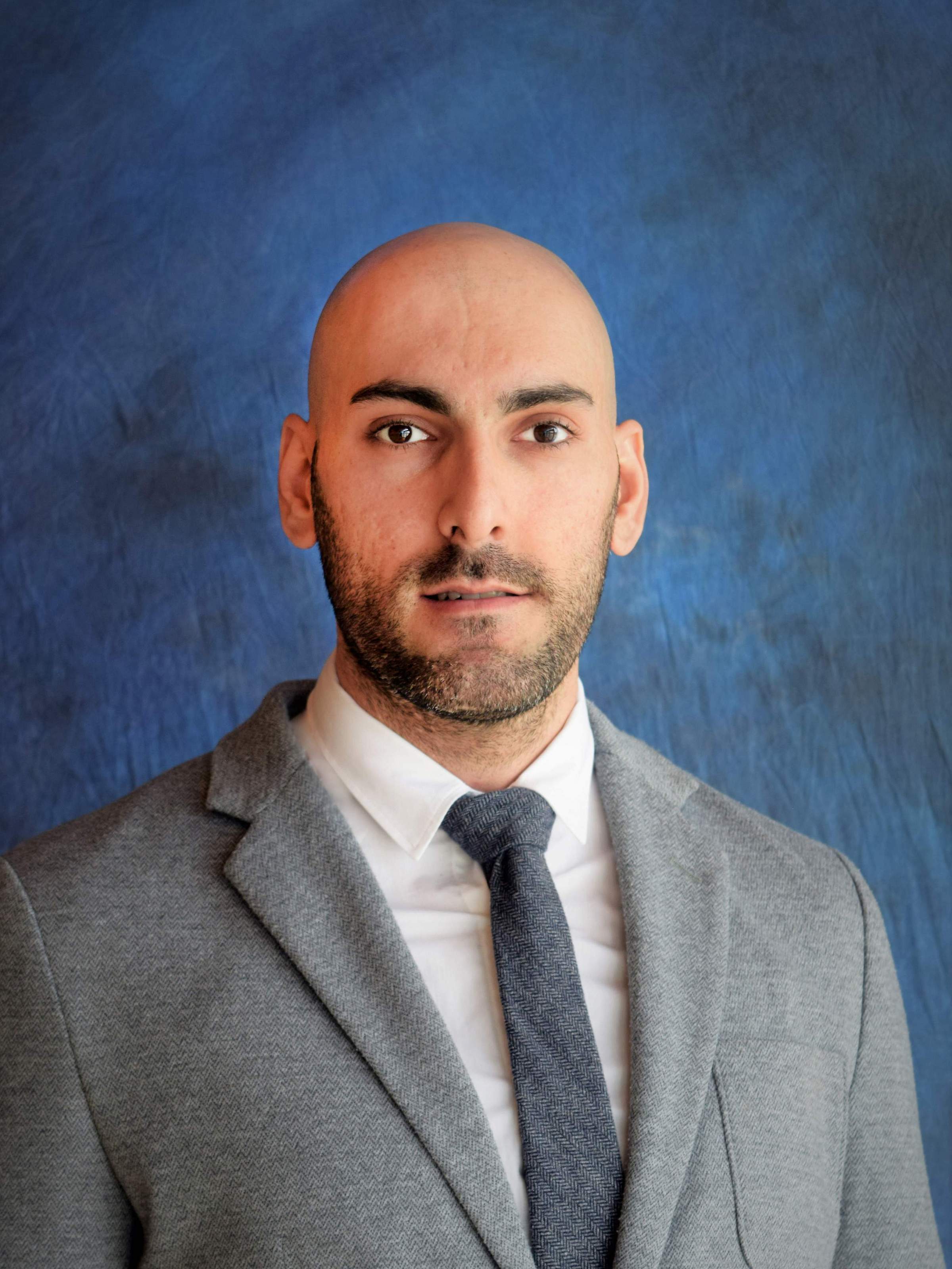Profile photo of a person in a suit in front of a blue background.