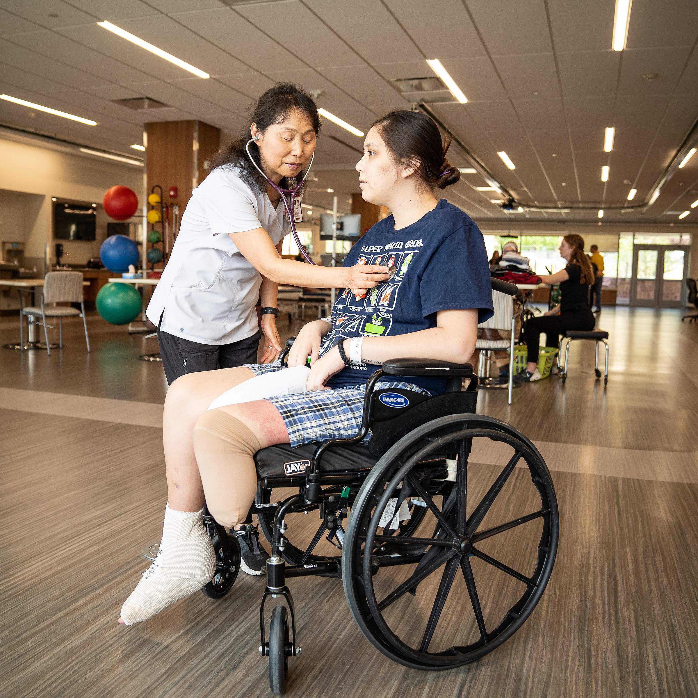 U of U Health rehab nurse listens to heart rate of a younger female patient with an amputated leg in a wheelchair.
