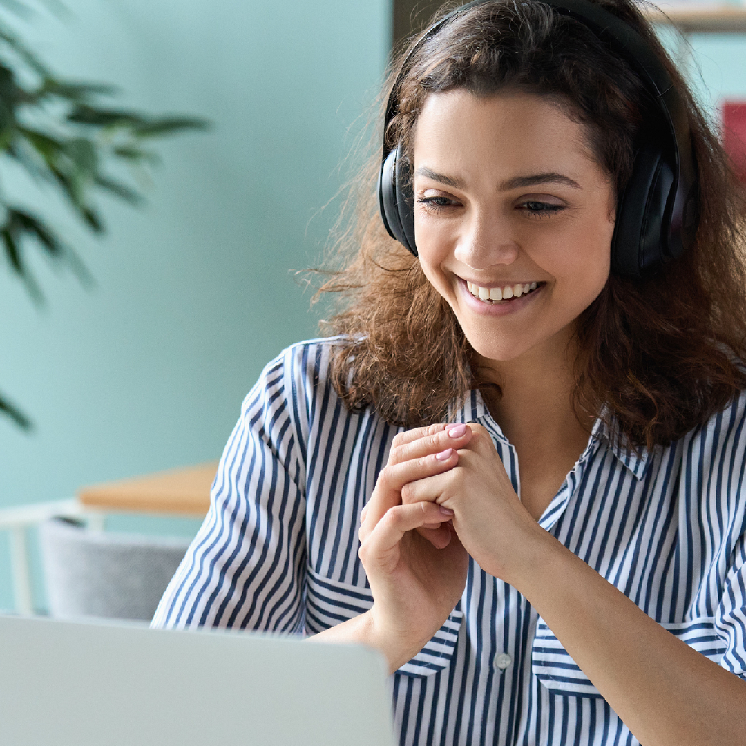 A woman wearing headphones and smiling at her laptop in a virtual call.